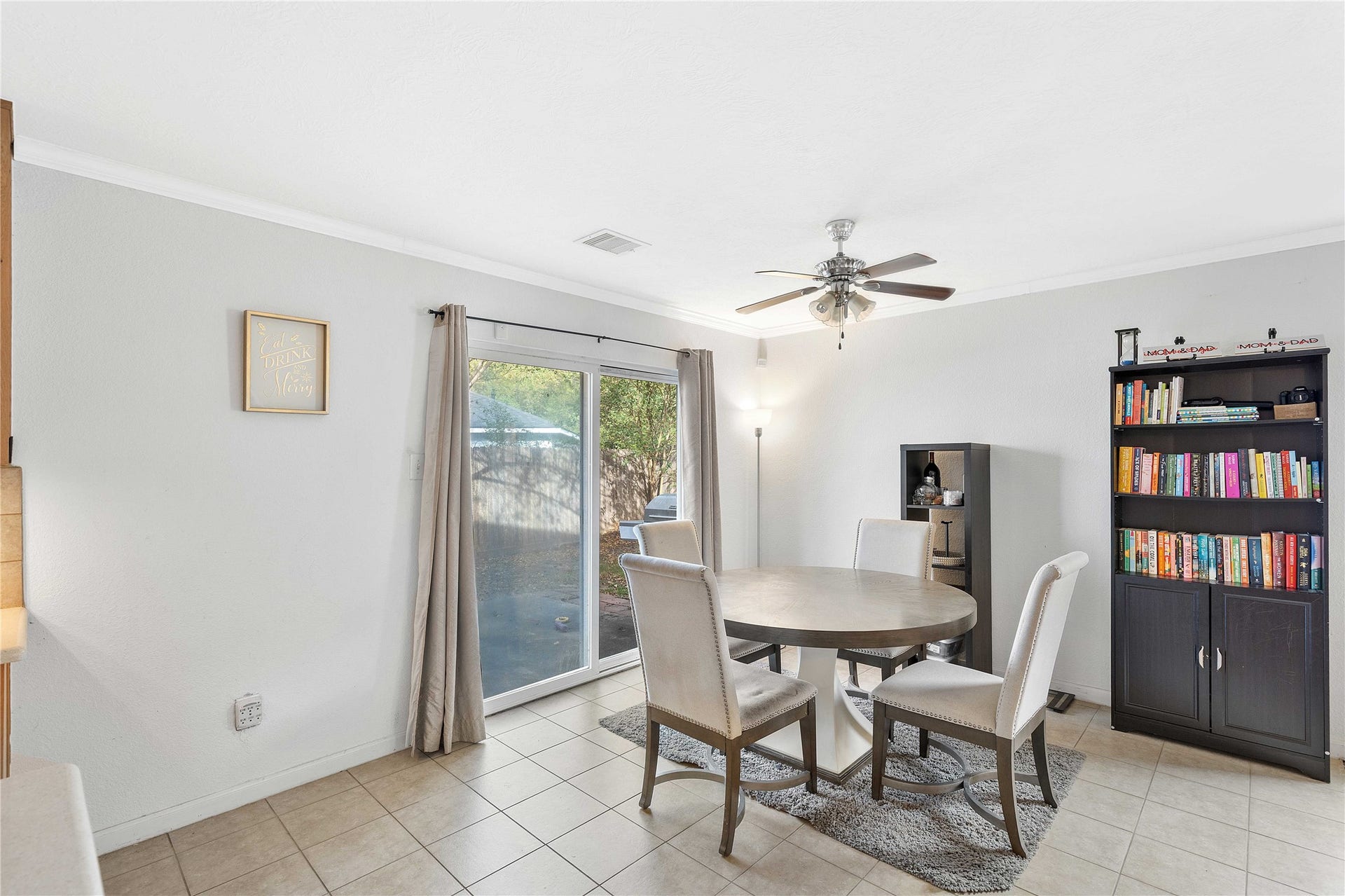 2910 Ribbon Creek Way, Spring, TX 77389 Bright dining area with tile flooring features a round table, comfortable chairs, and a ceiling fan. A large sliding glass door offers access to a serene backyard, while a bookshelf adds charm and functionality.