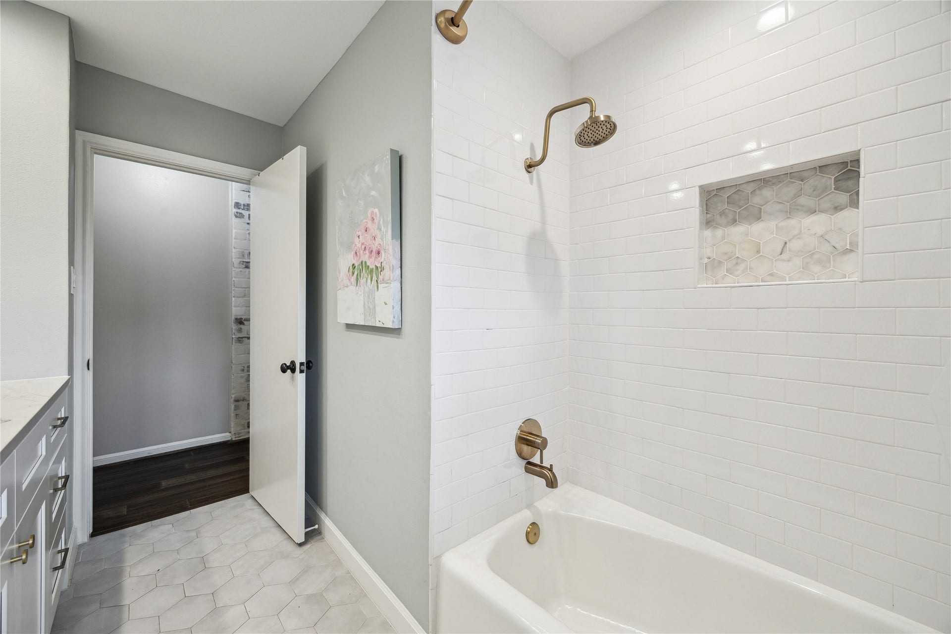 10714 Piping Rock Lane, Houston, TX 77042 White subway tile, a recessed storage niche and brass-tone fixtures surround the combination tub and shower.