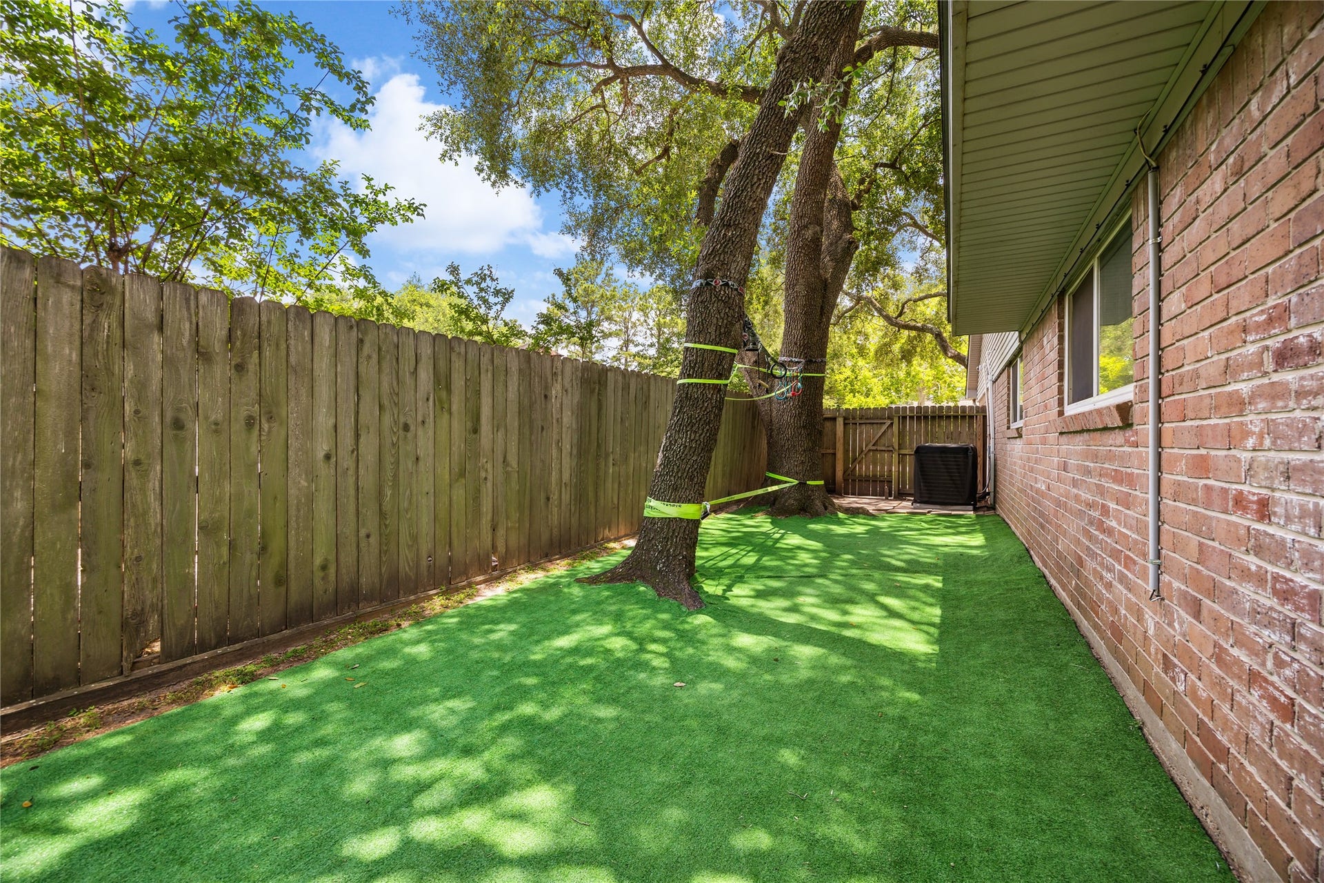 10714 Piping Rock Lane, Houston, TX 77042 A fenced side yard features a green ground covering and shade from a mature tree, extending the homes usable outdoor space.