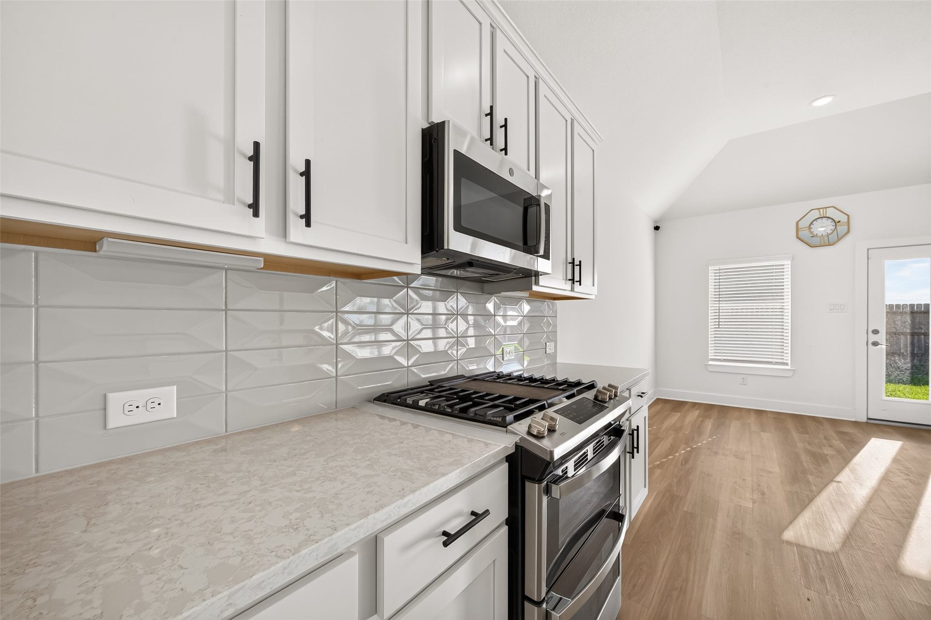 2002 Flatland Drive, Rosenberg, TX 77471 Gas range and stainless steel microwave with white shaker-style cabinets, decorative tile backsplash, and light countertops.