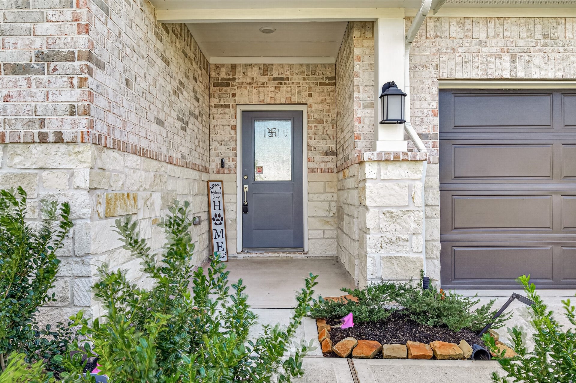 2002 Flatland Drive, Rosenberg, TX 77471 Covered front entry with brick and stone accents, glass-paneled front door, coach light, and landscaped beds.