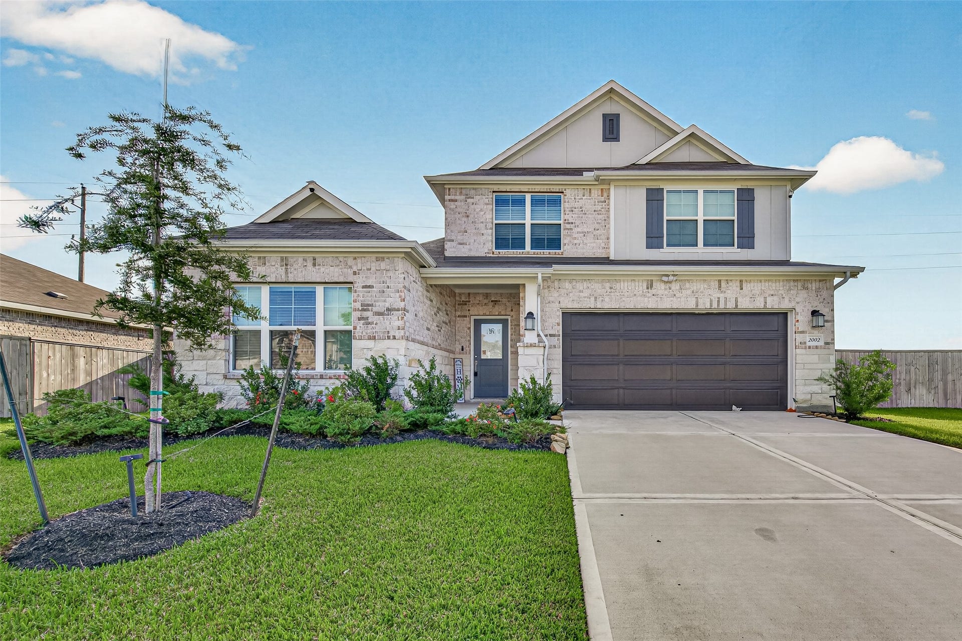 2002 Flatland Drive, Rosenberg, TX 77471 Front exterior with landscaped lawn, young shade tree, and wide driveway.