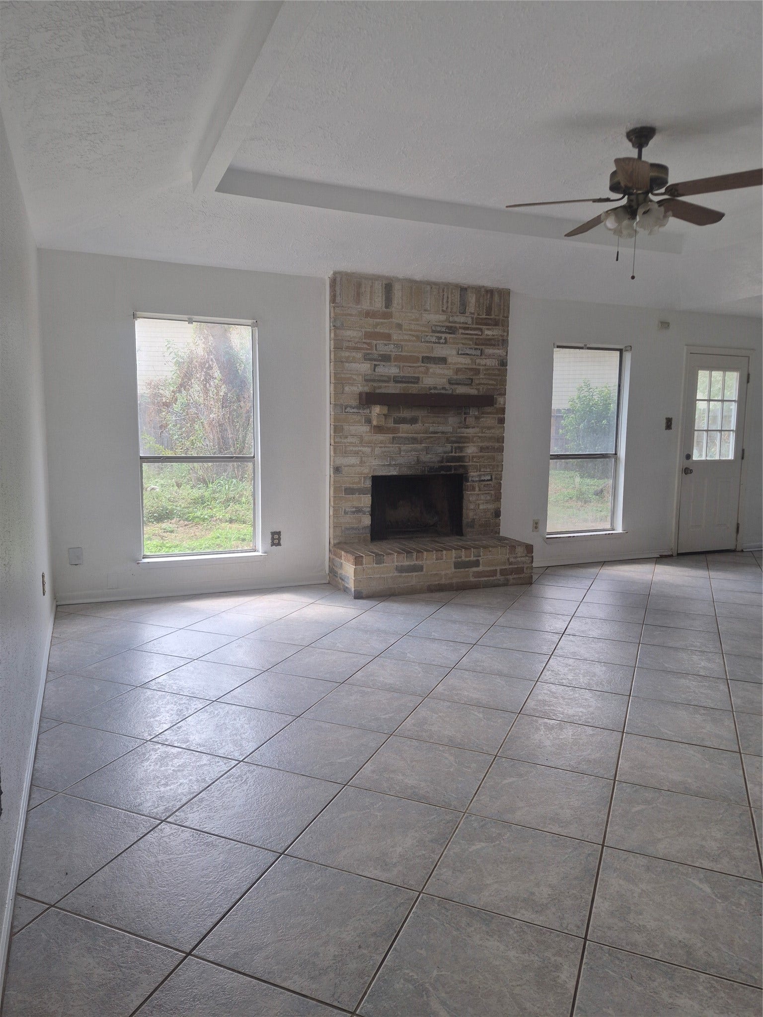 10603 Village Trail Drive, Houston, TX 77065 Spacious living area with a brick fireplace, tile flooring, and natural light from two large windows.