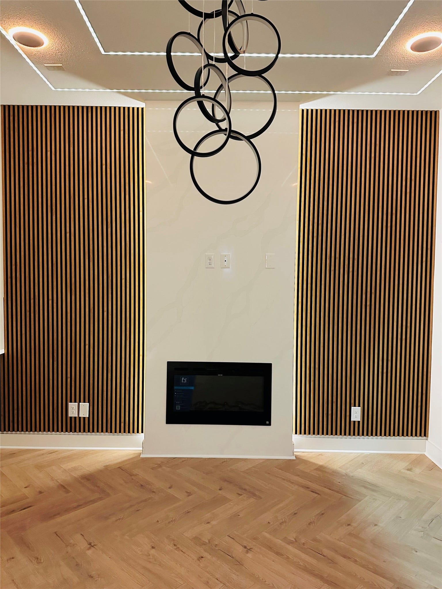 Living room in unit A & B Feature High ceilings, Smart App controlled Electric fireplace that can be connected to smart home device, 3CM quartz wall accented by slatwall panels. Height adjustable LED chandelier accented by recessed smart led lights to create the perfect ambiance in any season of life.