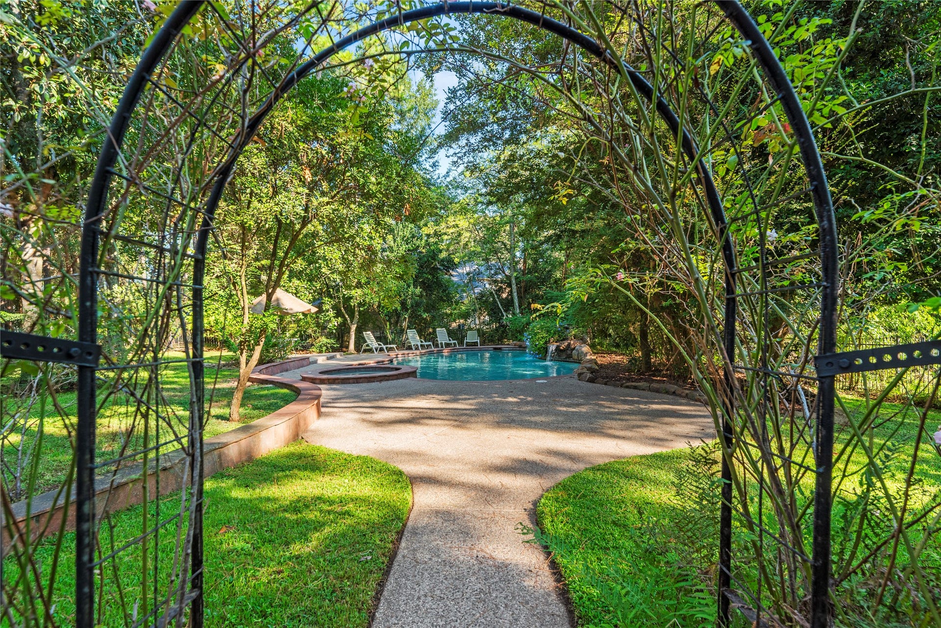 A garden arbor creates a charming entrance to the secluded backyard pool, surrounded by mature trees and lush landscaping.