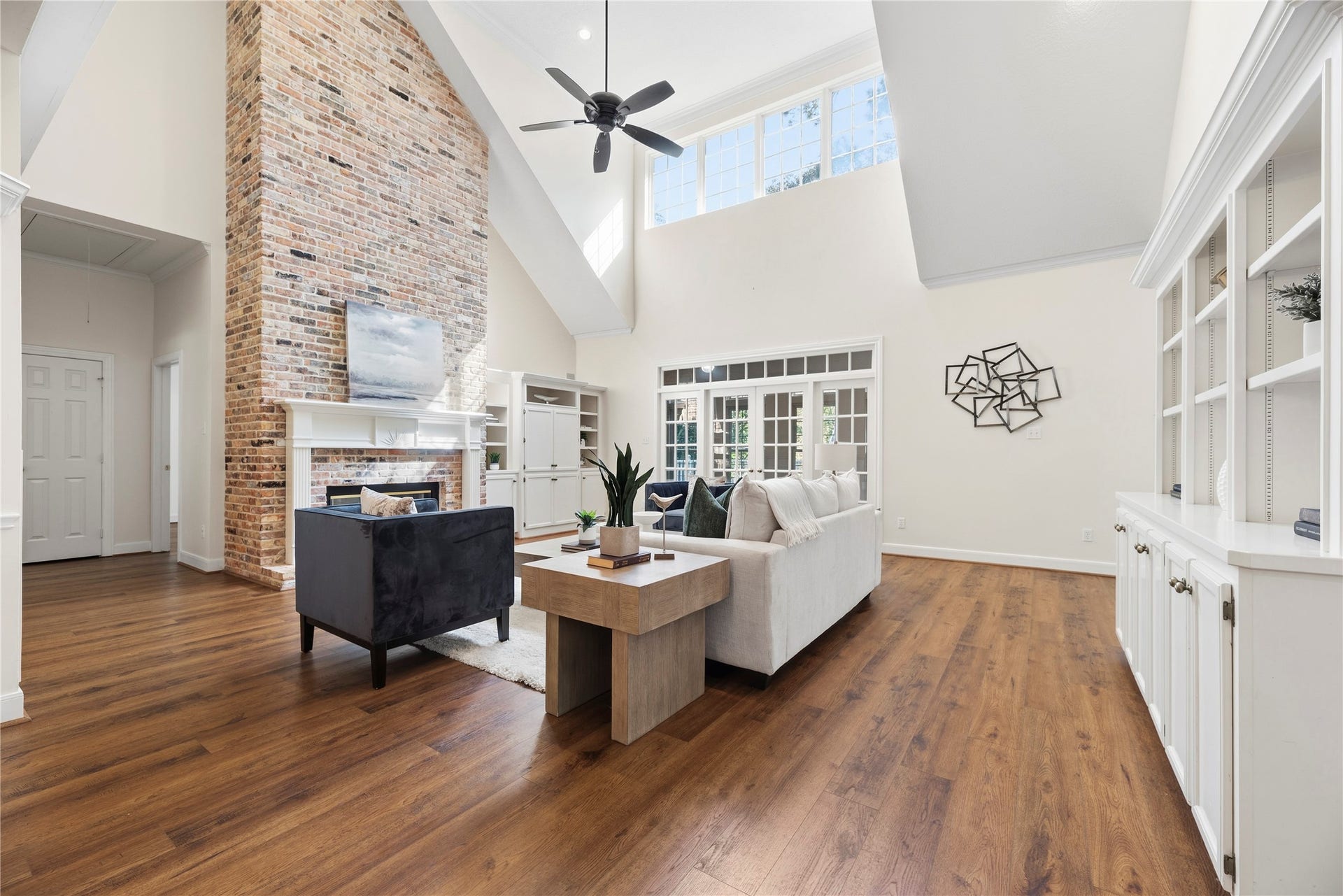 Soaring ceilings and a dramatic brick fireplace create a striking focal point in the main living area, complemented by built-in cabinetry and warm wood floors.