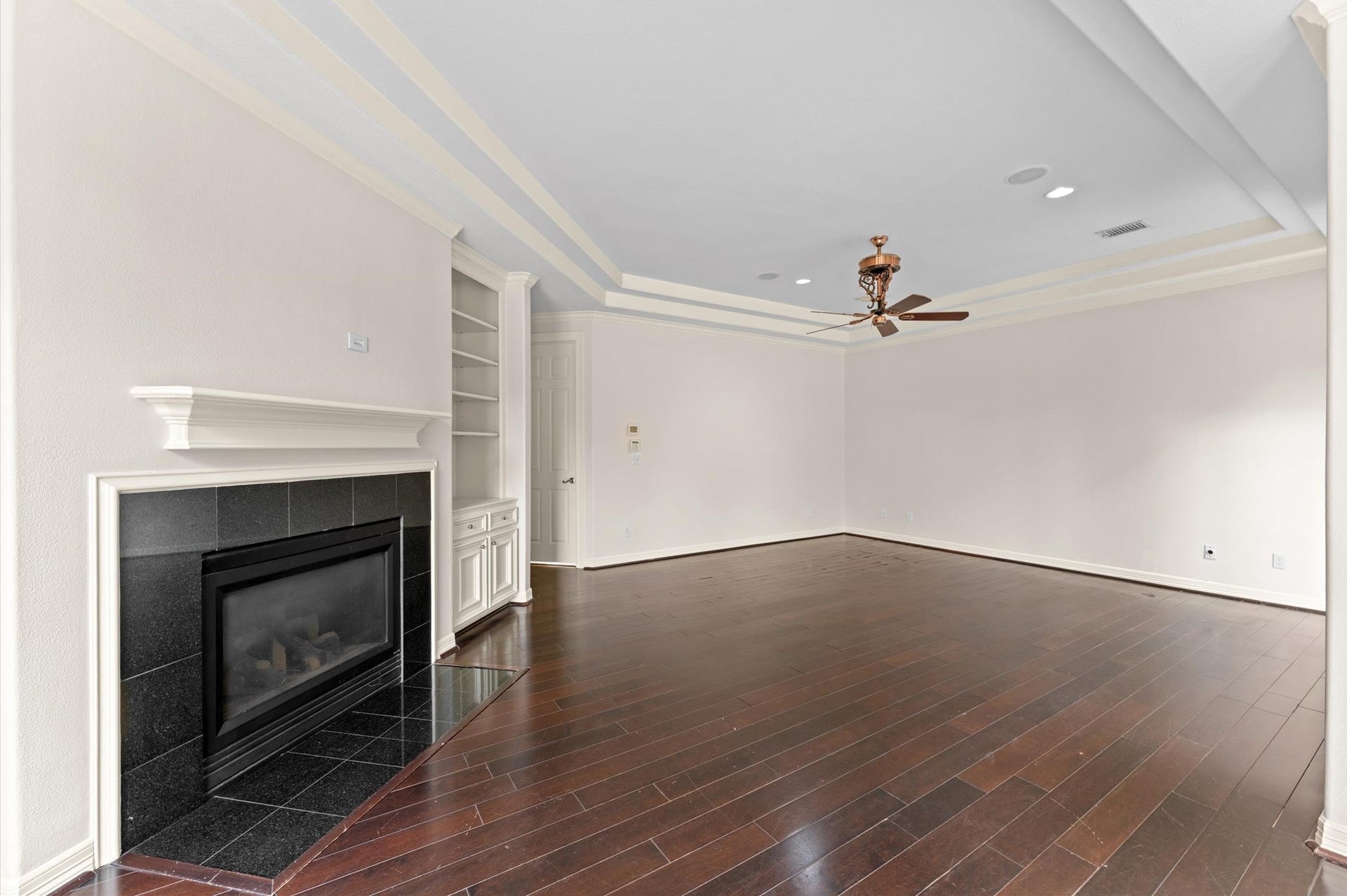 1830 Forest Gate Circle, Sugar Land, TX 77479 This view of the primary bedroom, highlights a gas fireplace with mantle, built-in bookcase, wood flooring and tray ceiling.