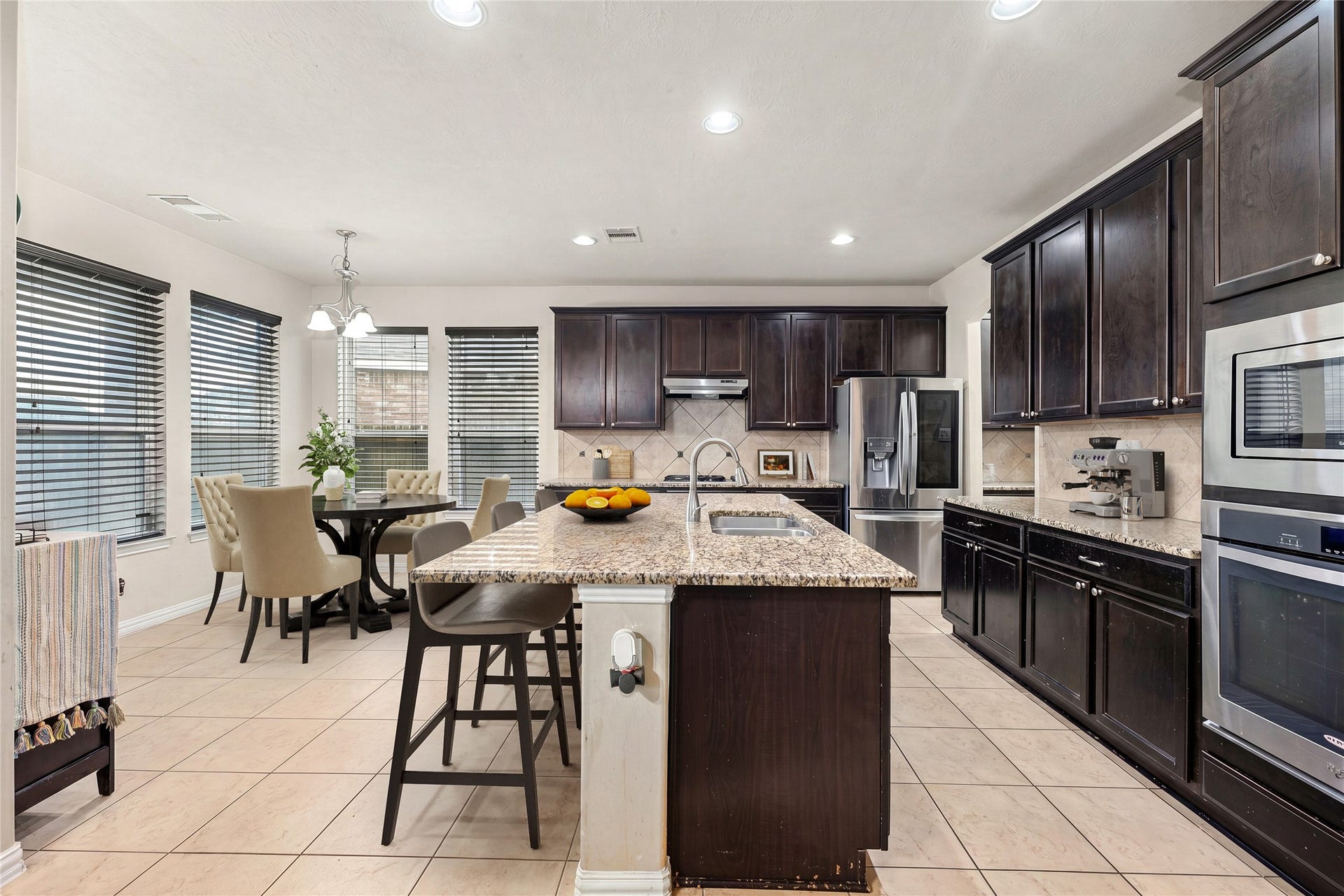 7018 Pearl Terrace Lane, Richmond, TX 77469 Bright, open kitchen with a granite island, bar seating, and stainless steel appliances, including built-in double ovens, flowing into a sunny breakfast area framed by oversized windows. *Virtually Staged