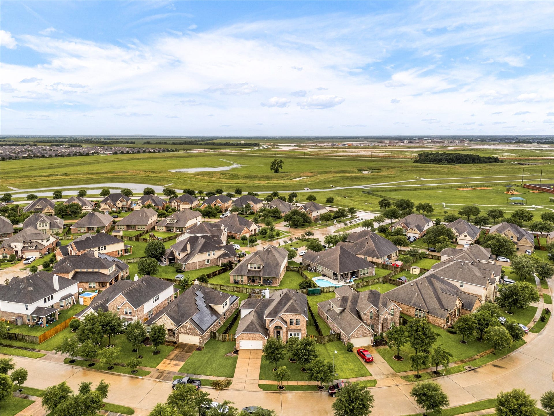 7018 Pearl Terrace Lane, Richmond, TX 77469 Striking aerial view showcasing the home's classic brick elevation, detached two-car garage, manicured landscaping, and an extended driveway, set in an established, family-friendly neighborhood with open green space nearby.