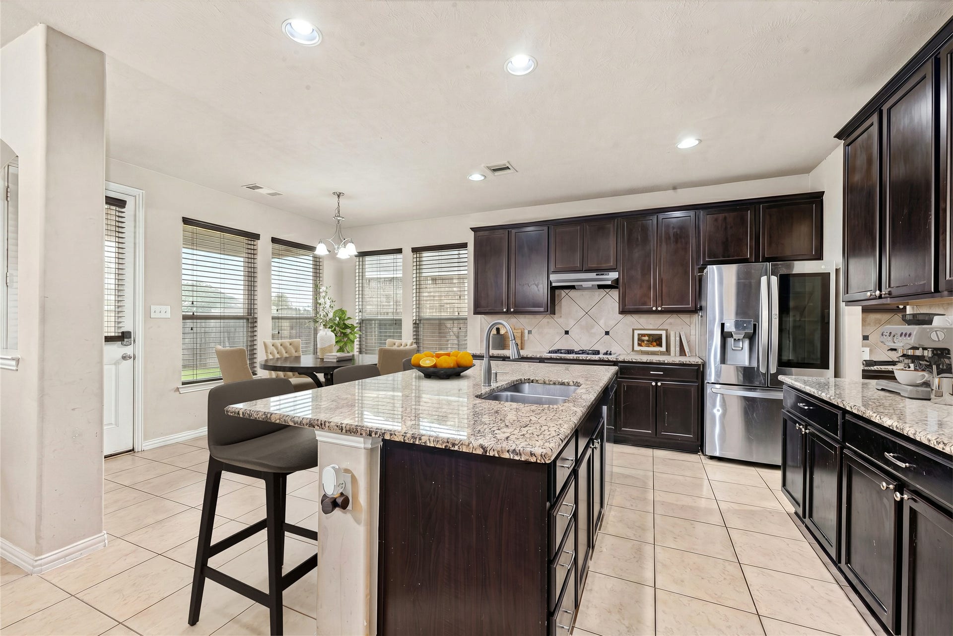7018 Pearl Terrace Lane, Richmond, TX 77469 Open-concept kitchen with granite-topped island seating, stainless steel appliances, gas cooktop, and a sunny breakfast nook framed by a bay of windows. *Virtually Staged