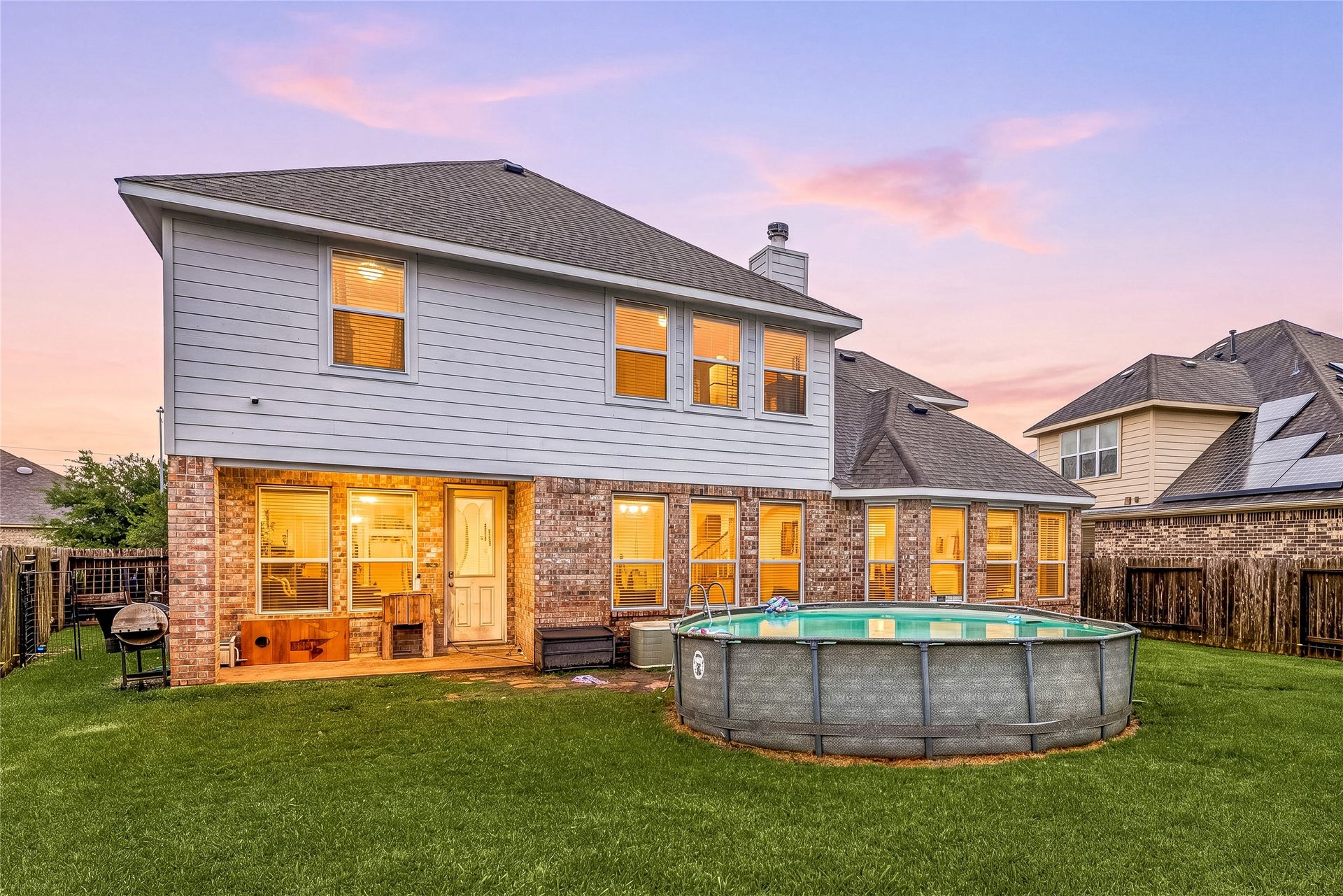 7018 Pearl Terrace Lane, Richmond, TX 77469 Stunning twilight view of the home's brick-and-siding rear elevation, with a covered patio, warm glowing interiors, and a spacious fenced backyard, perfect for relaxing and entertaining as the sun sets.