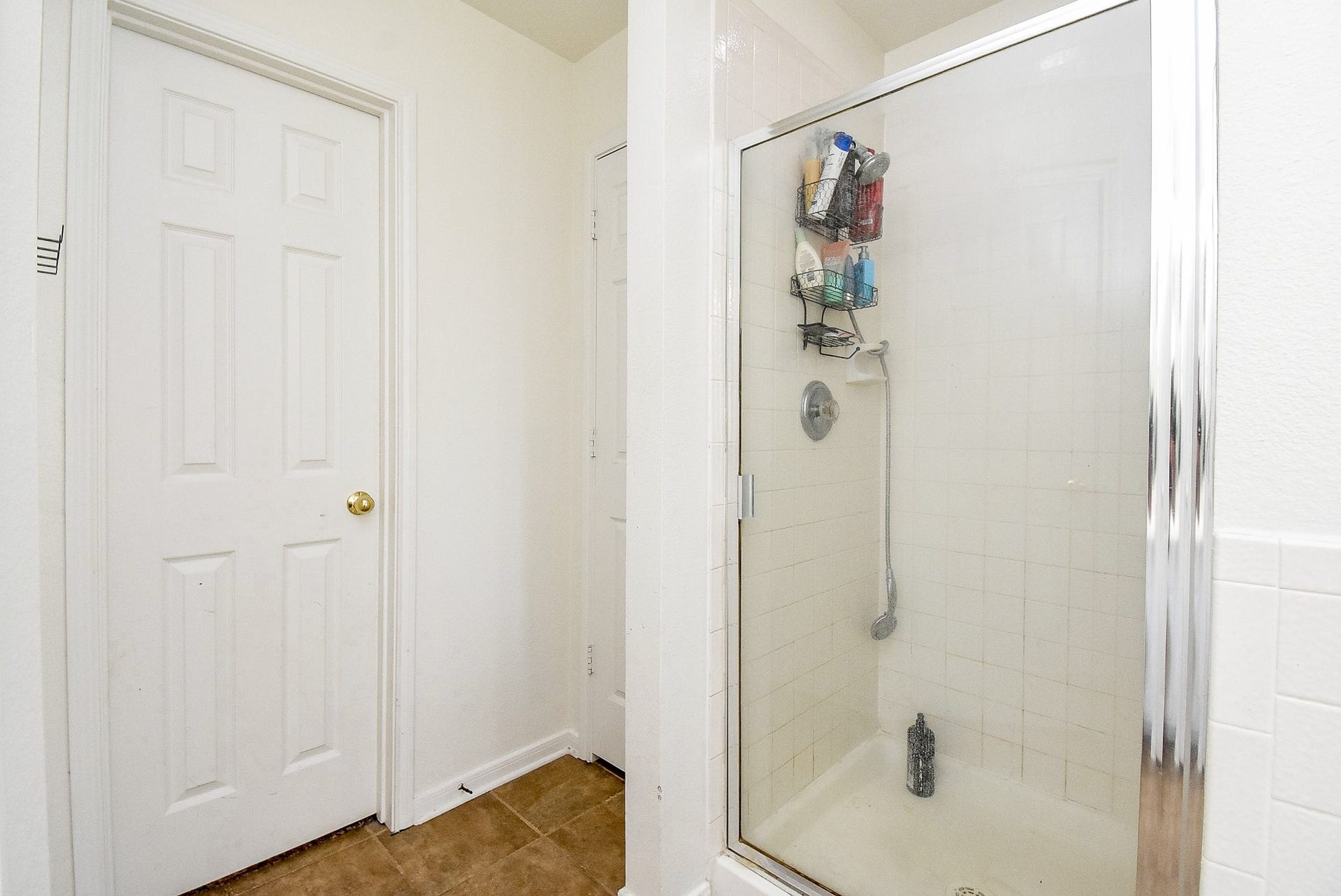 6703 Morning Glory Trace, Richmond, TX 77407 This bathroom features a glass-enclosed shower with white tile and a handheld showerhead. There's a door adjacent to the shower, and the space is finished with neutral tile flooring, creating a clean and functional design.