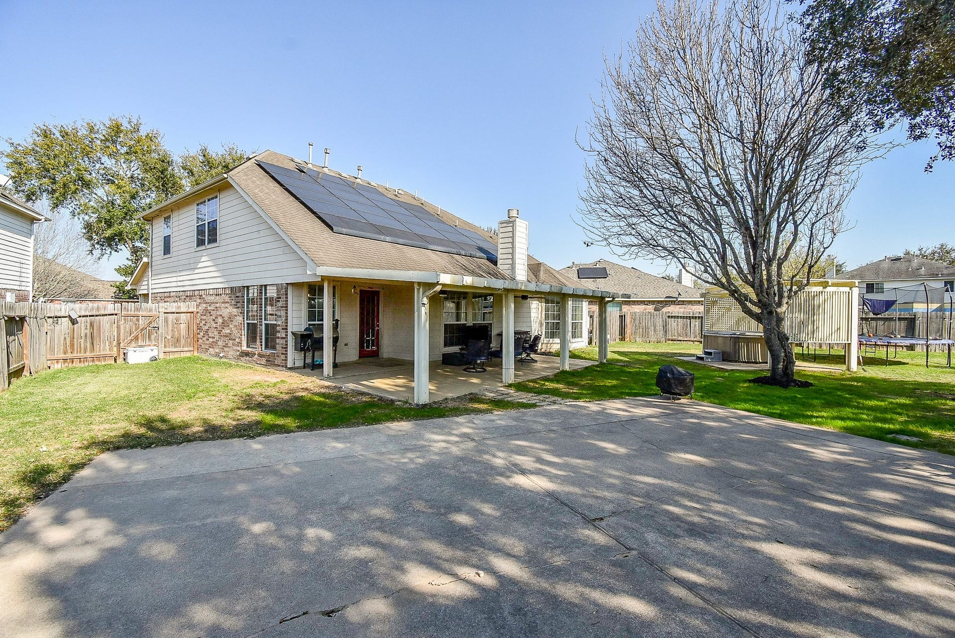 6703 Morning Glory Trace, Richmond, TX 77407 This photo showcases a spacious backyard featuring a two-story home with solar panels on the roof. The yard includes a covered patio, mature trees, and a fenced perimeter, providing ample space for outdoor activities.
