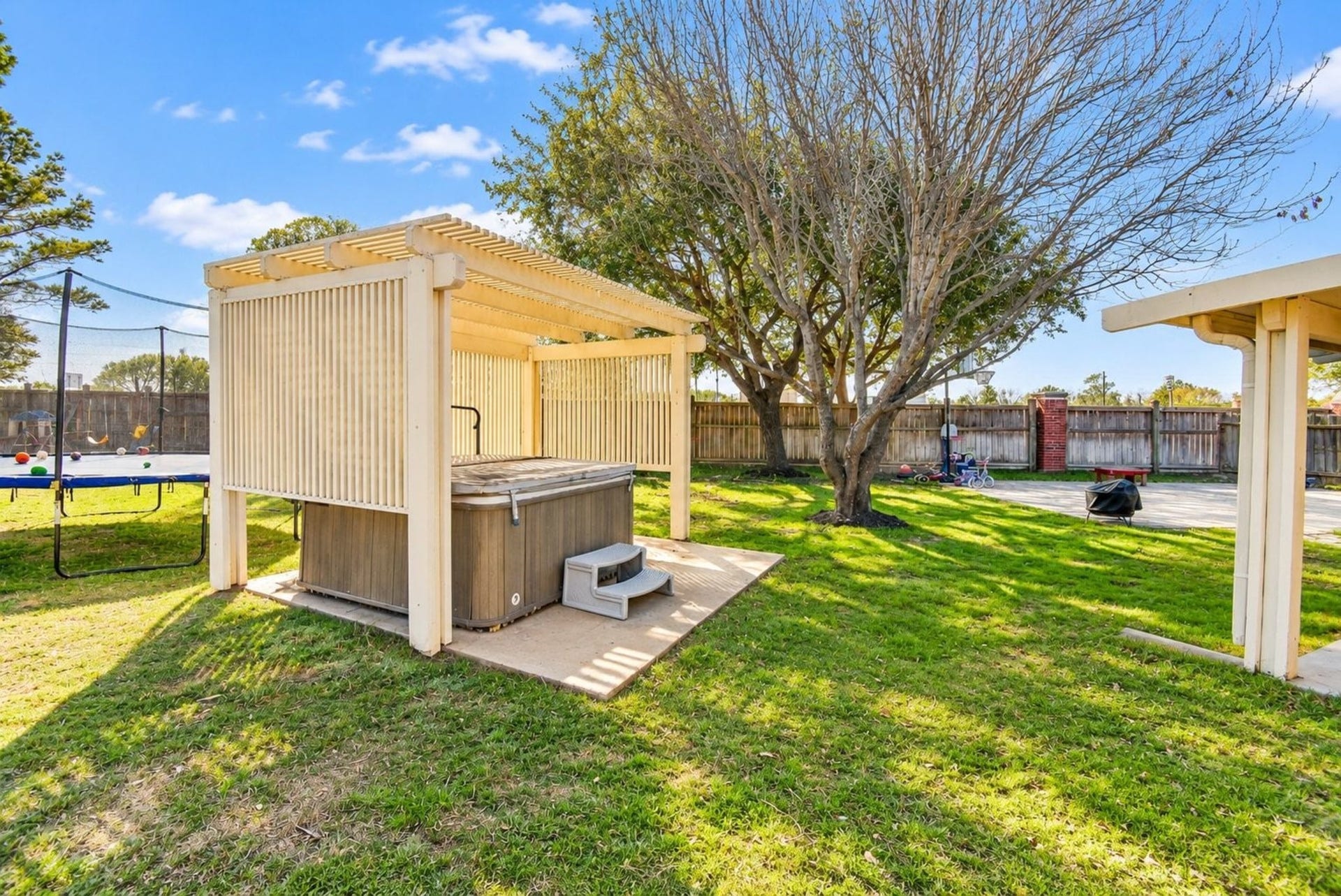 6703 Morning Glory Trace, Richmond, TX 77407 This backyard features a covered hot tub area with a pergola, a trampoline, and a spacious lawn, perfect for relaxation and outdoor activities.