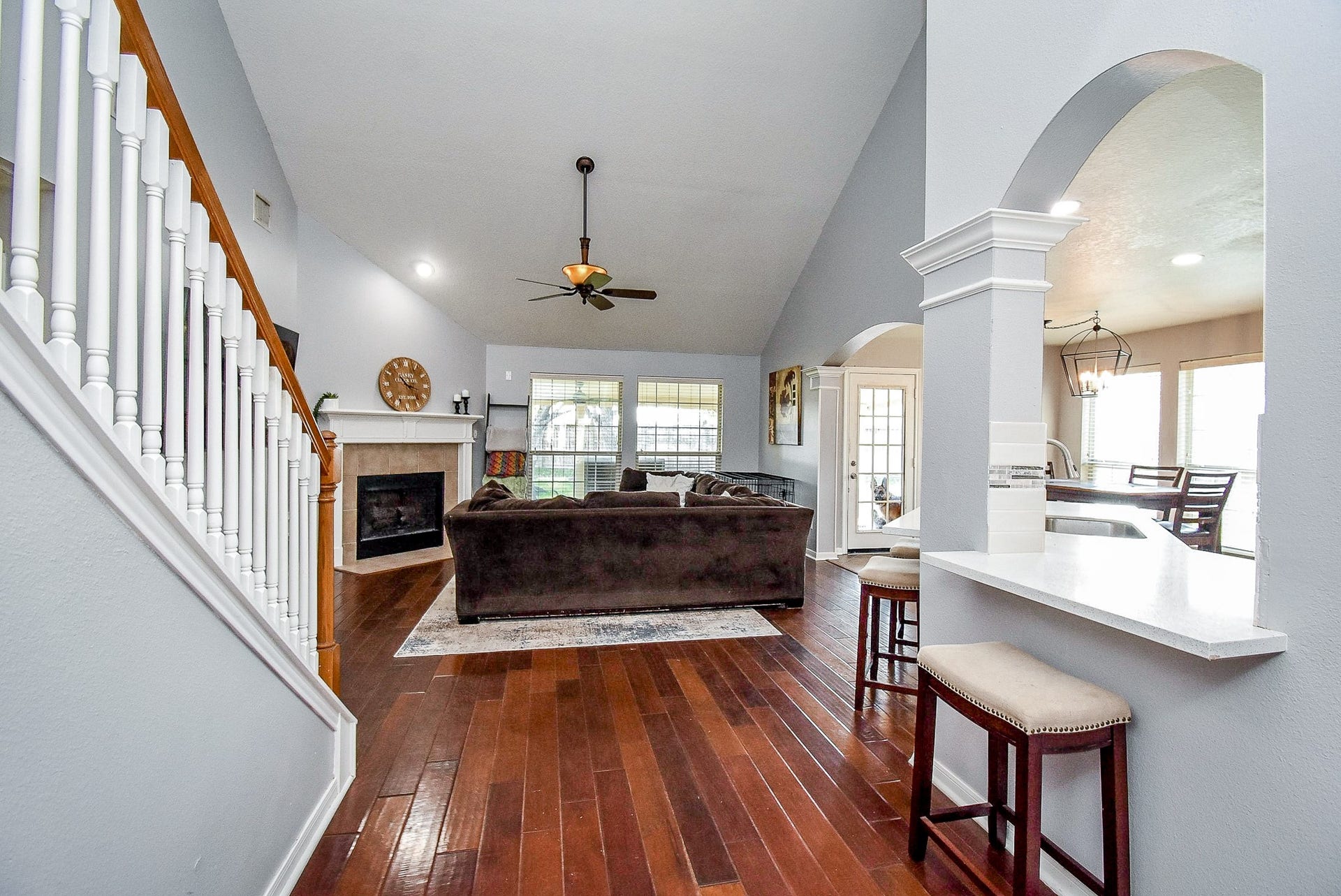 6703 Morning Glory Trace, Richmond, TX 77407 Spacious living area with high ceilings, featuring a cozy fireplace and rich hardwood floors. The open layout includes a breakfast bar and dining area, accented by large windows for natural light.