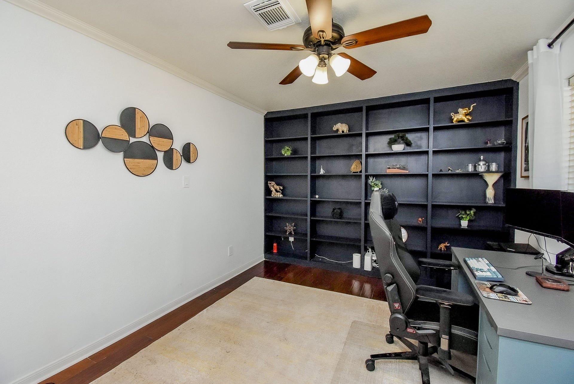 6703 Morning Glory Trace, Richmond, TX 77407 This photo showcases a modern home office with a sleek black shelving unit, decorative wall art, and a ceiling fan. The room has ample natural light and a comfortable workspace, making it ideal for productivity.