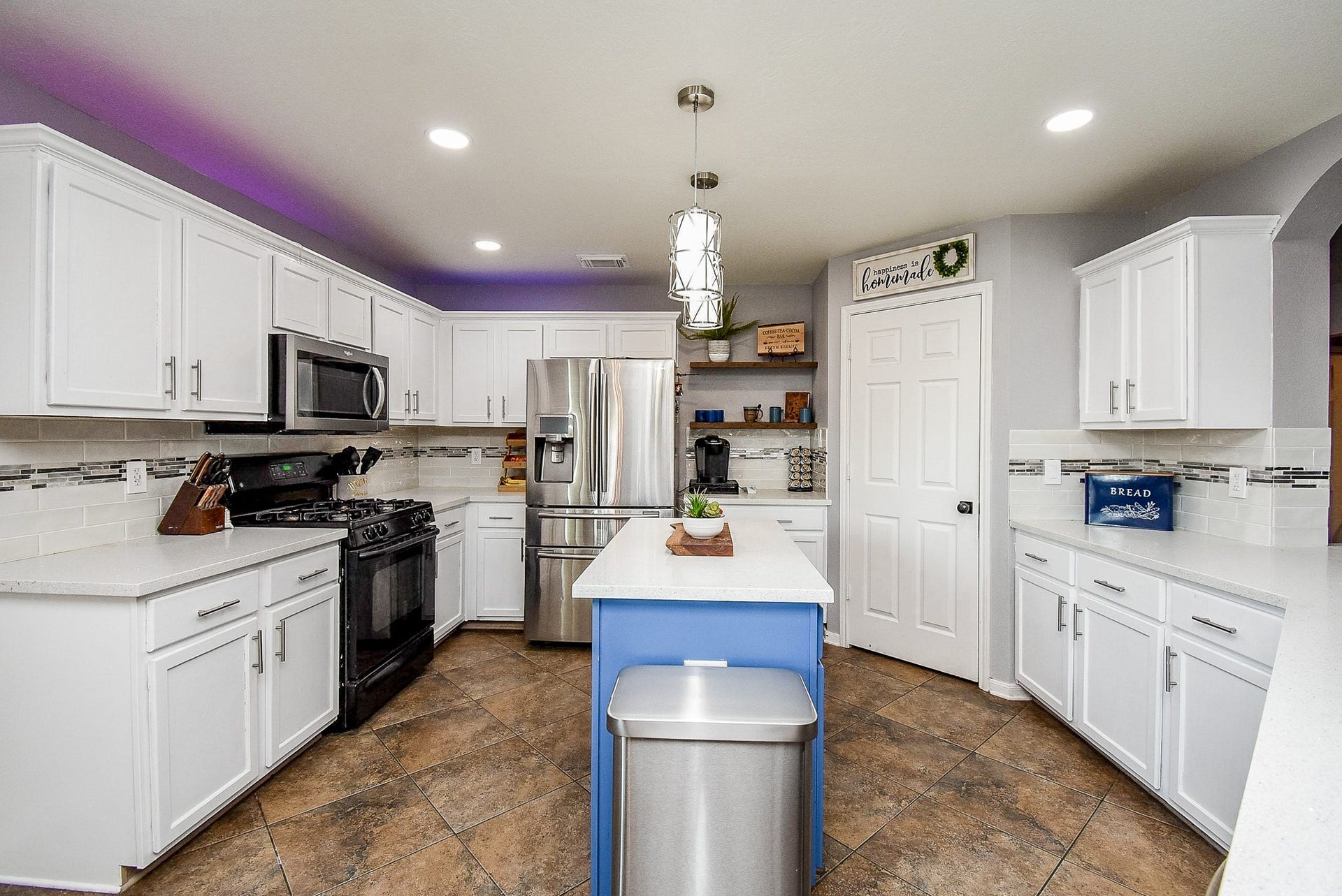 6703 Morning Glory Trace, Richmond, TX 77407 This modern kitchen features white cabinetry, stainless steel appliances, and a central island with a blue base. It has ample counter space, a stylish tile backsplash, and recessed lighting, creating a bright and inviting space.