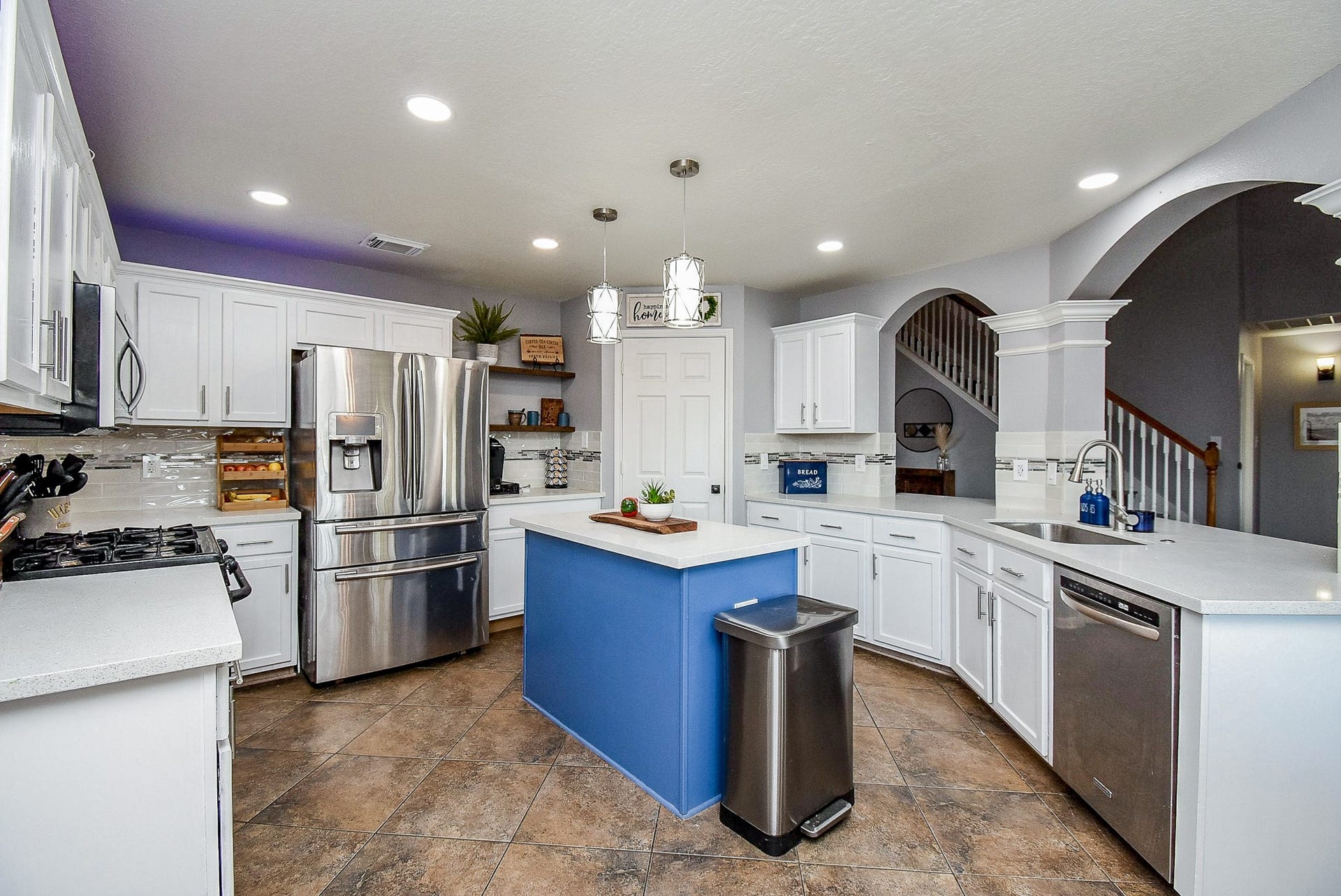 6703 Morning Glory Trace, Richmond, TX 77407 This kitchen features a modern design with white cabinetry, stainless steel appliances, and a striking blue island. It has ample counter space, recessed lighting, and a stylish backsplash, creating a bright and inviting cooking space.