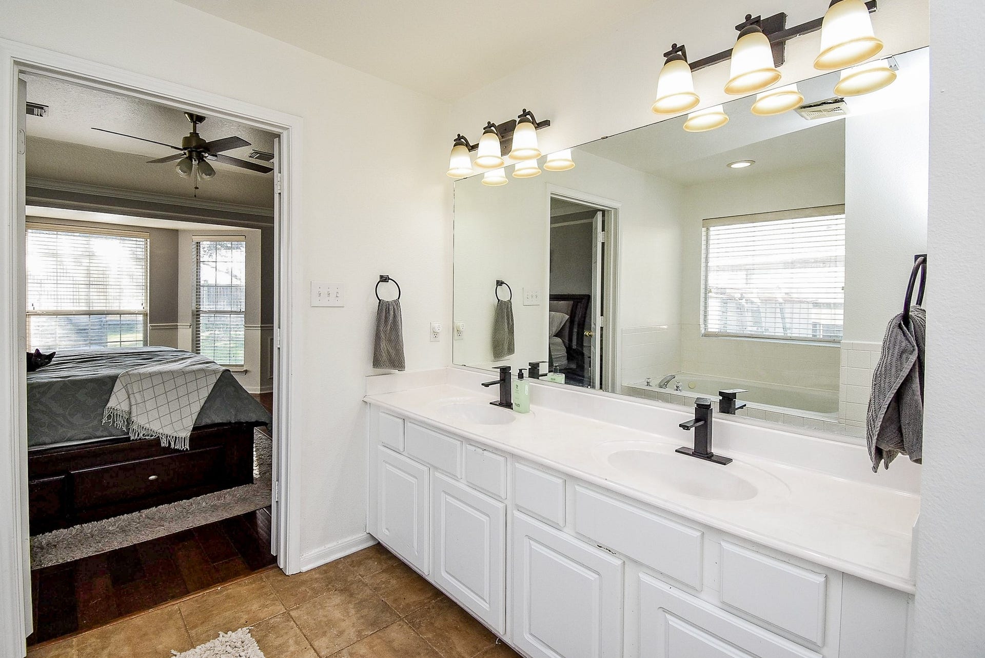 6703 Morning Glory Trace, Richmond, TX 77407 This photo showcases a bright bathroom with a large mirror, dual sinks, and modern fixtures. Adjacent to the bathroom is a bedroom with hardwood floors, a ceiling fan, and ample natural light from multiple windows.