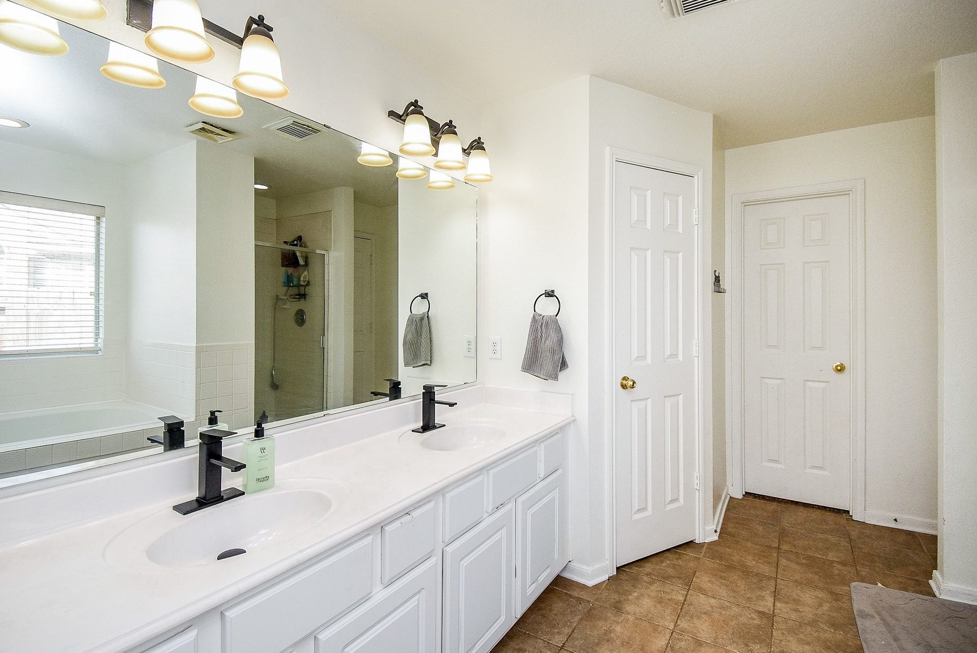 6703 Morning Glory Trace, Richmond, TX 77407 This bathroom features a spacious layout with a double vanity, modern black fixtures, ample lighting, and a separate shower and bathtub area. The neutral tones and tile flooring add a clean, contemporary feel.