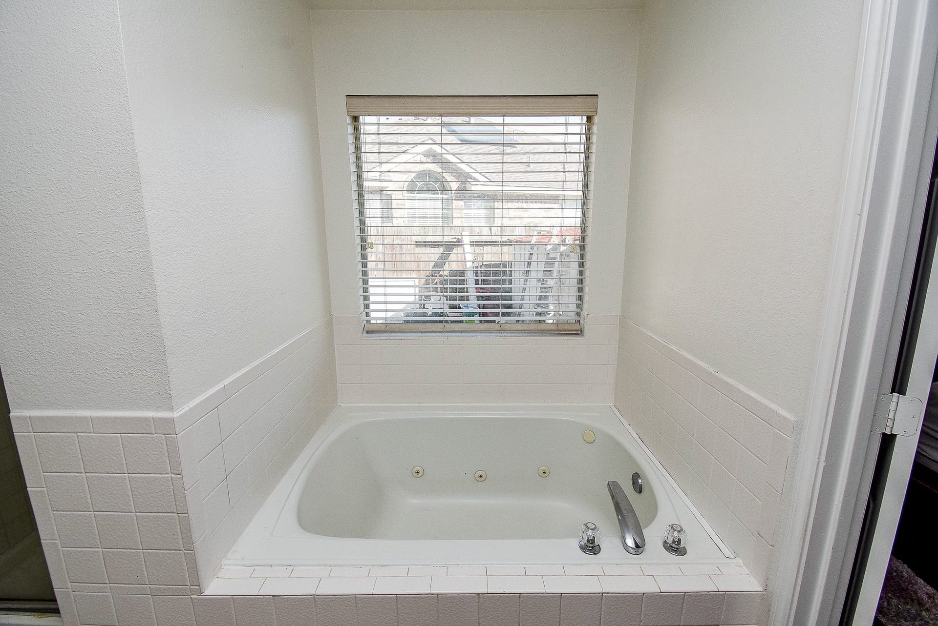 6703 Morning Glory Trace, Richmond, TX 77407 This bathroom features a cozy, white-tiled jacuzzi tub with jets, positioned under a window with blinds, offering a relaxing space with natural light.
