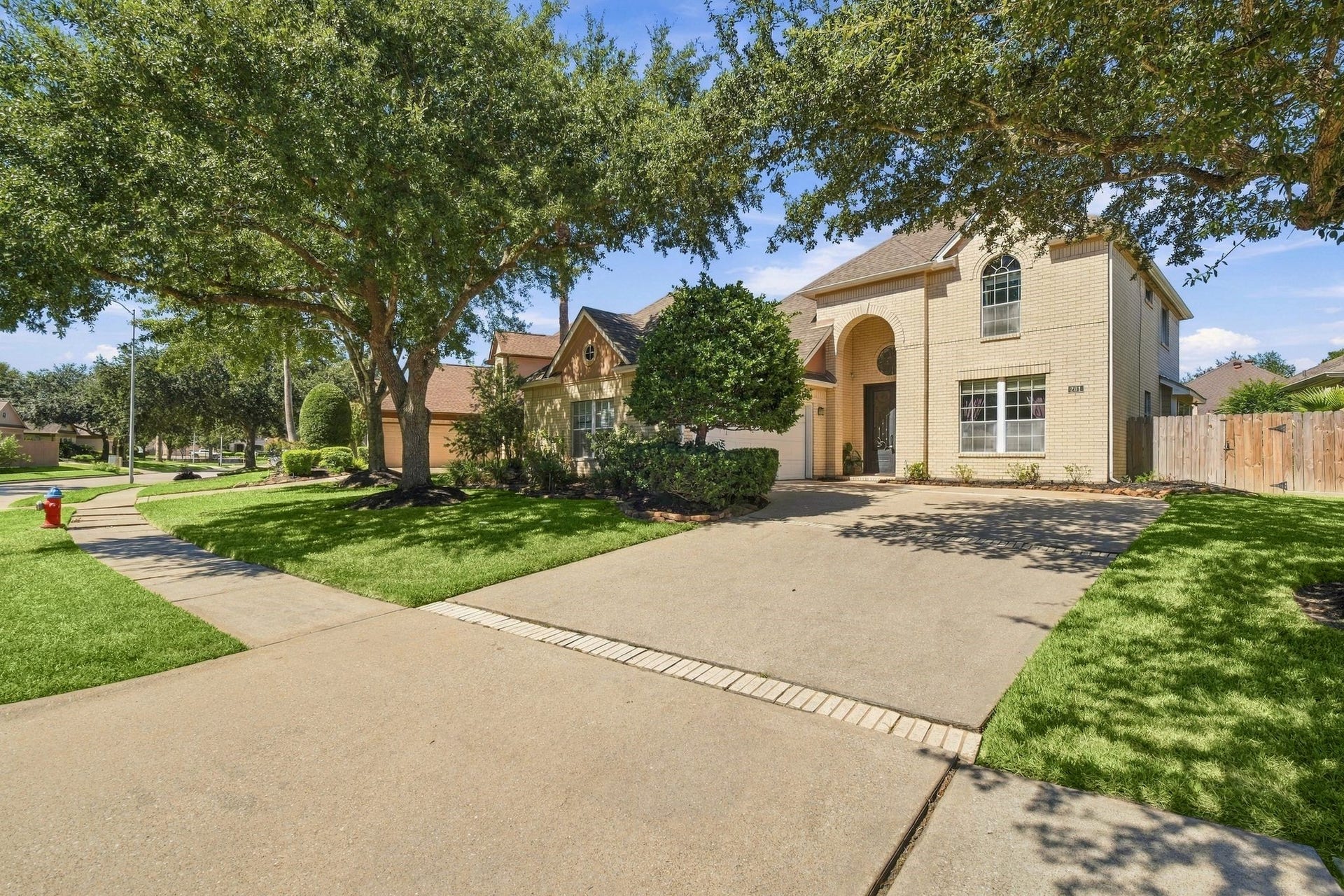 201 Lago Vista Street, League City, TX 77565 Charming home with a spacious driveway leading to a convenient two-car garage, nestled amid lush greenery.