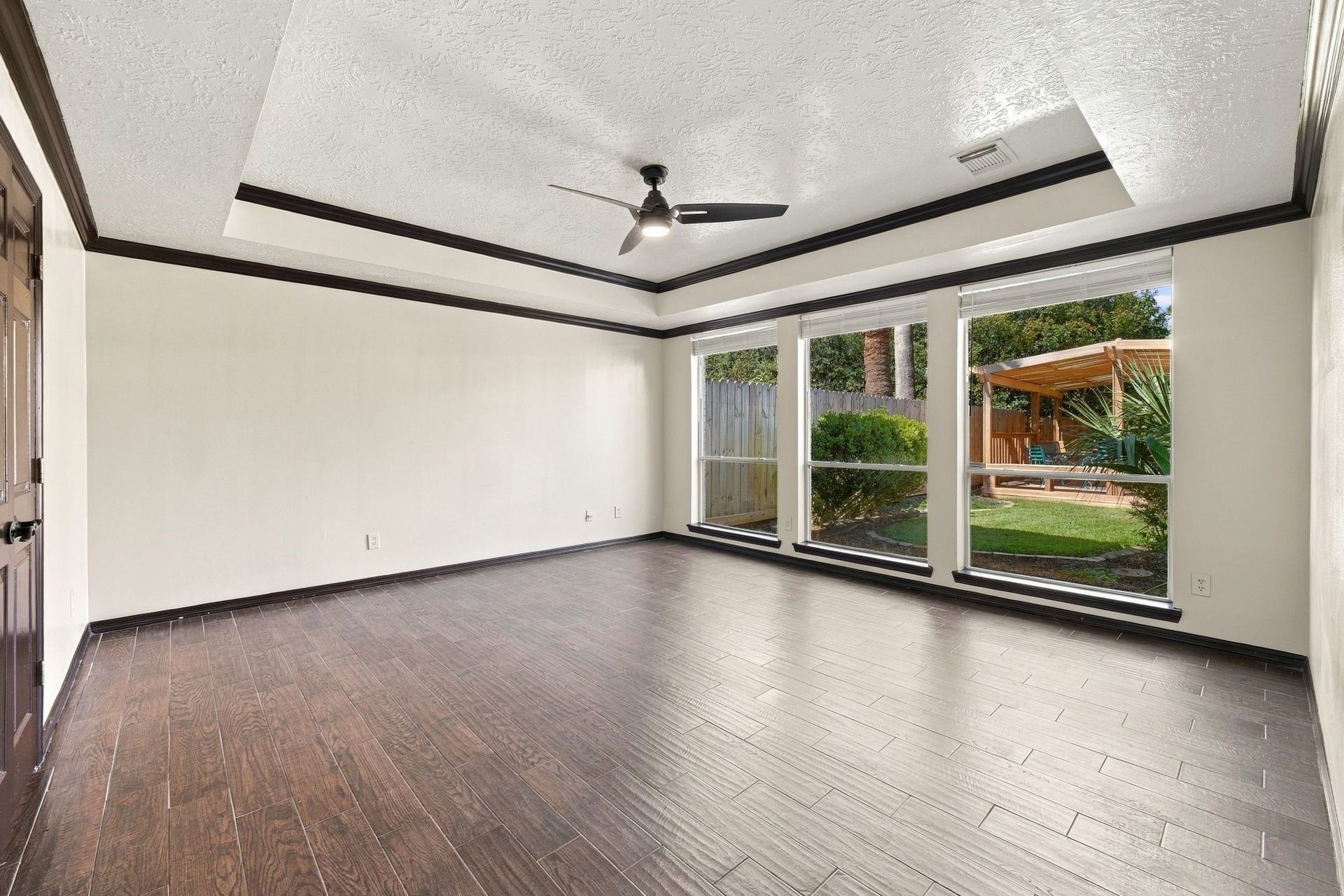 201 Lago Vista Street, League City, TX 77565 Discover the potential in this unstaged room, featuring elegant wood flooring, a modern ceiling fan, and expansive windows that offer a serene view of the lush backyard oasis.