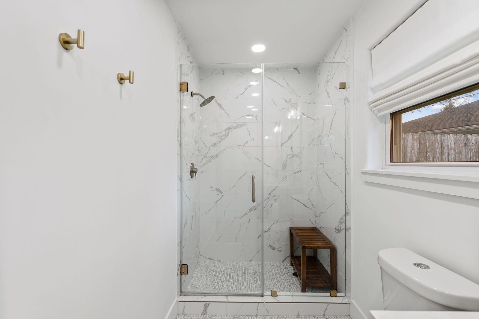 9206 Kapri Lane, Houston, TX 77025 Updated bathroom showcases a spacious glass-enclosed shower with floor-to-ceiling marble-look tile, pebble-style shower flooring, rainfall shower-head and contemporary fixtures.