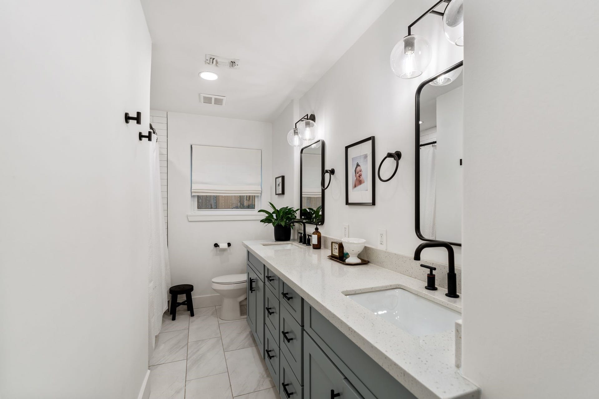 9206 Kapri Lane, Houston, TX 77025 Updated full bath features a long double-sink vanity, generous counter space, modern black fixtures, contemporary lighting, framed mirrors and large-format tile flooring.