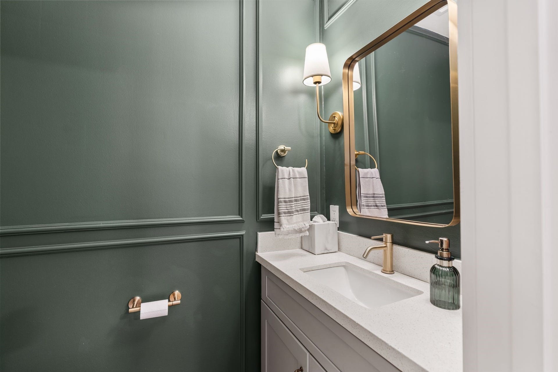 9206 Kapri Lane, Houston, TX 77025 Stylish powder room features rich paneled walls, a streamlined vanity with quartz-style countertop, undermount sink, brushed-gold fixtures, framed mirror and elegant wall-sconce lighting.