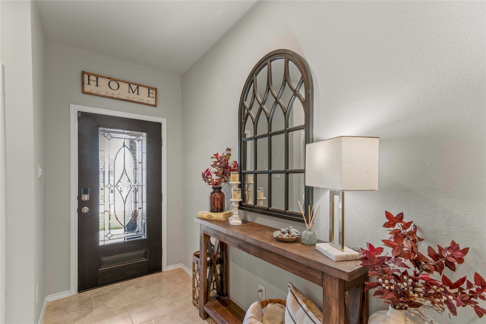 Charming entryway with a decorative glass front door, elegant mirror, and a stylish console table adorned with tasteful decor, creating a warm and inviting atmosphere.