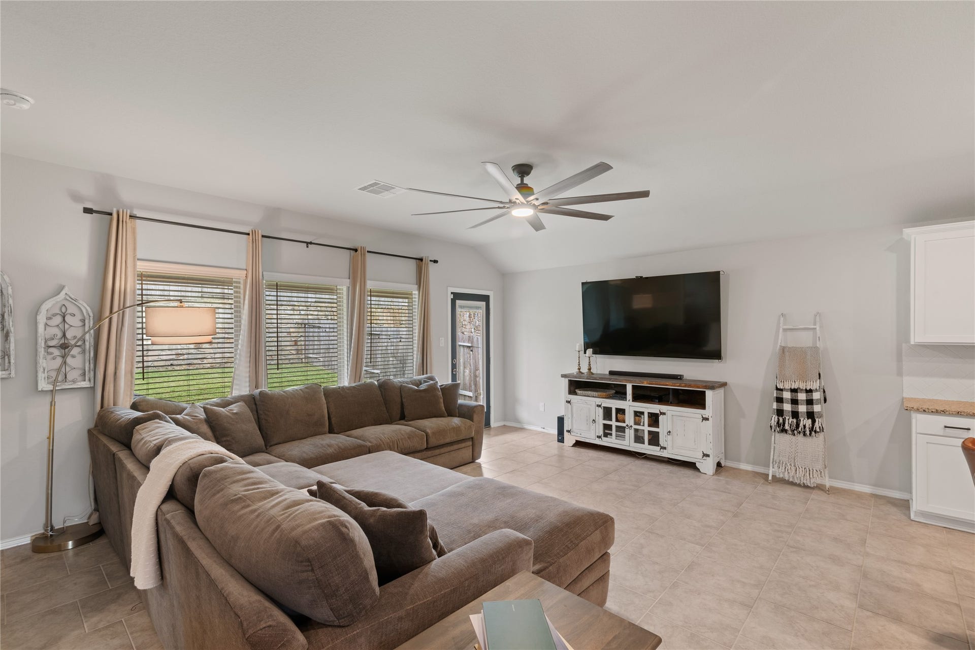 Spacious living room featuring a cozy sectional sofa, large windows with natural light, and a sleek ceiling fan, perfect for relaxation and entertainment.
