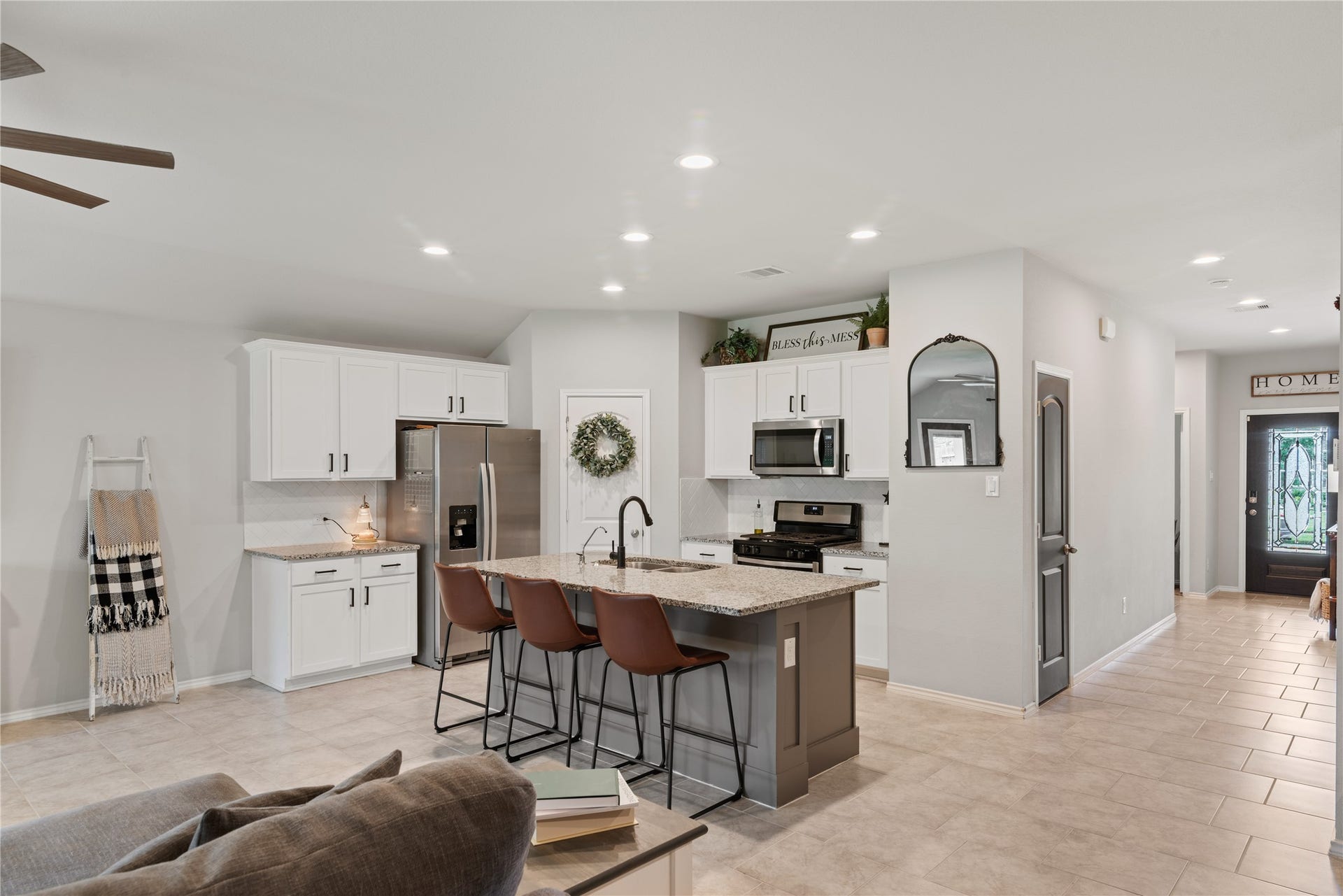 Spacious open-plan kitchen with modern white cabinetry, stainless steel appliances, and a central island with seating, seamlessly connecting to a welcoming entryway.