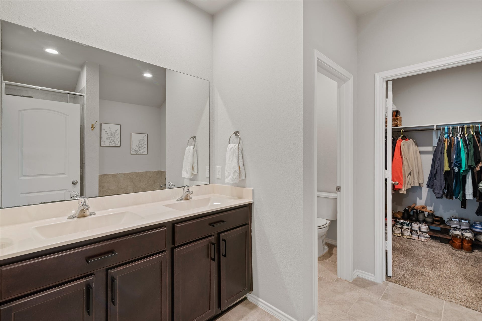 Spacious bathroom featuring a double vanity with elegant dark wood cabinets, leading to a walk-in closet with ample storage space.