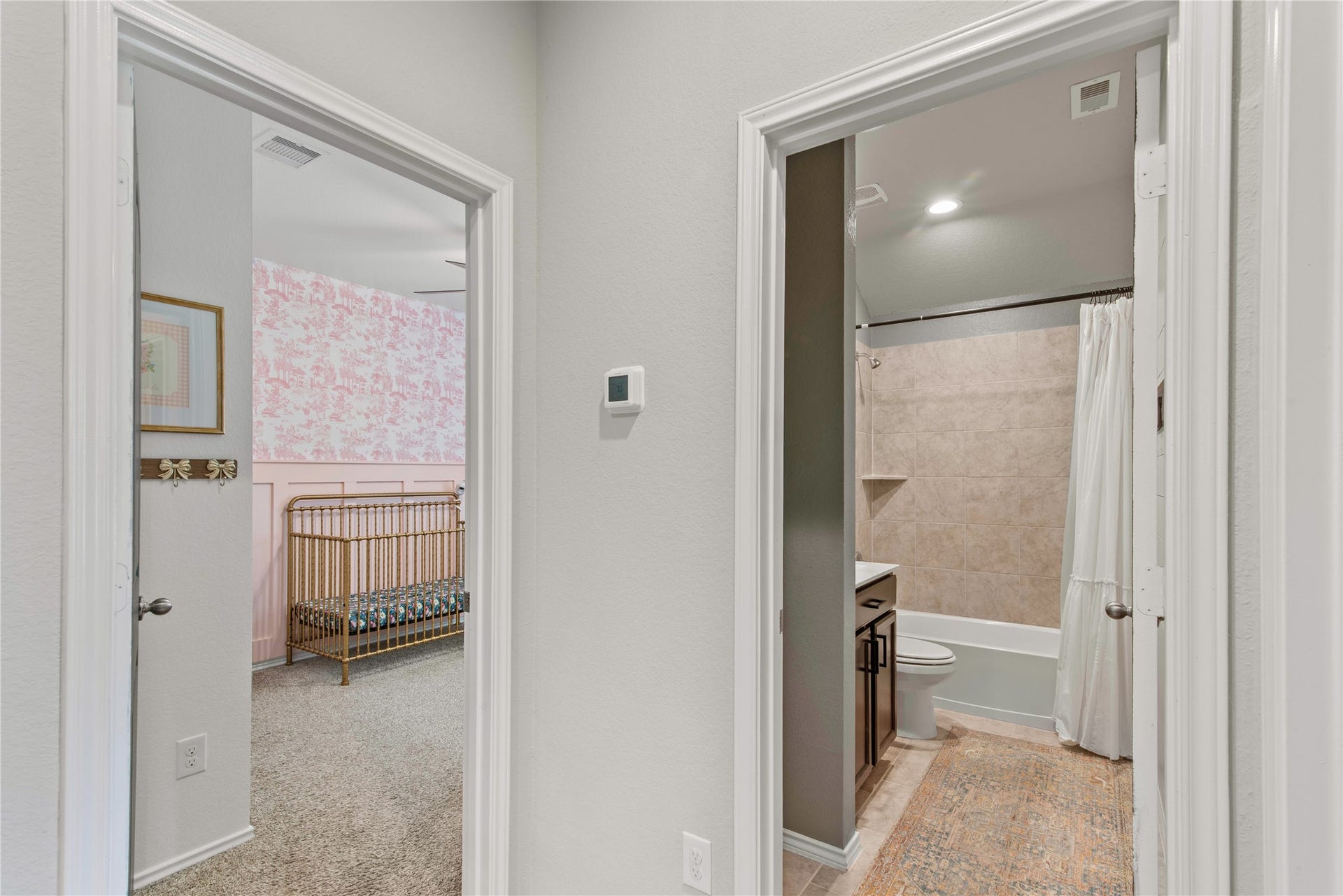 Charming hallway leads to a cozy nursery with pink wallpaper and a sleek bathroom featuring a modern tub and shower.