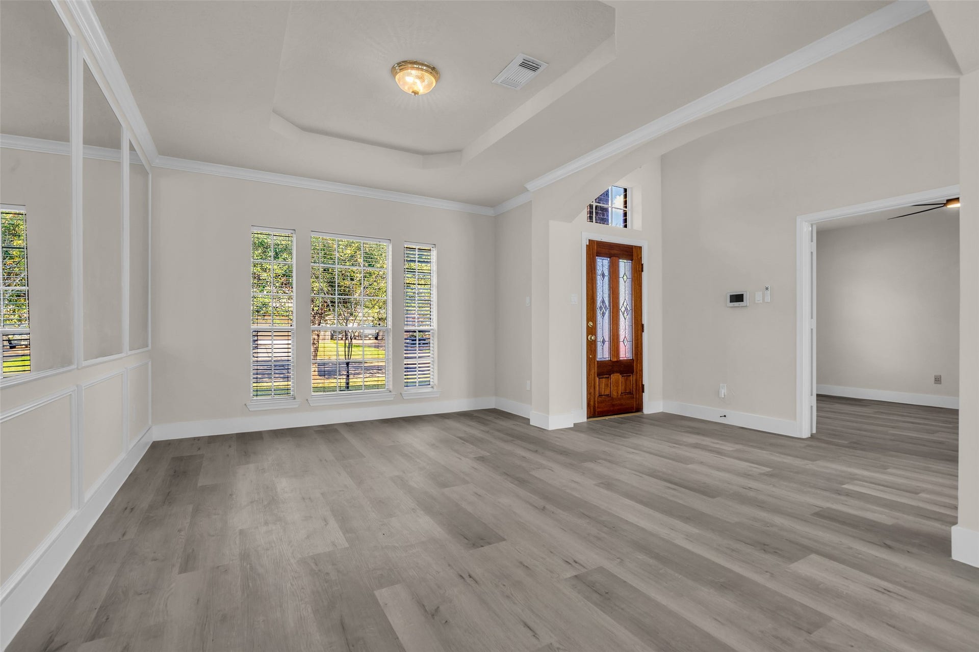 6110 Four River Drive, Richmond, TX 77469 Bright and inviting entryway featuring elegant tray ceilings, large windows for natural light, and sleek wood flooring, complemented by a classic wooden front door.