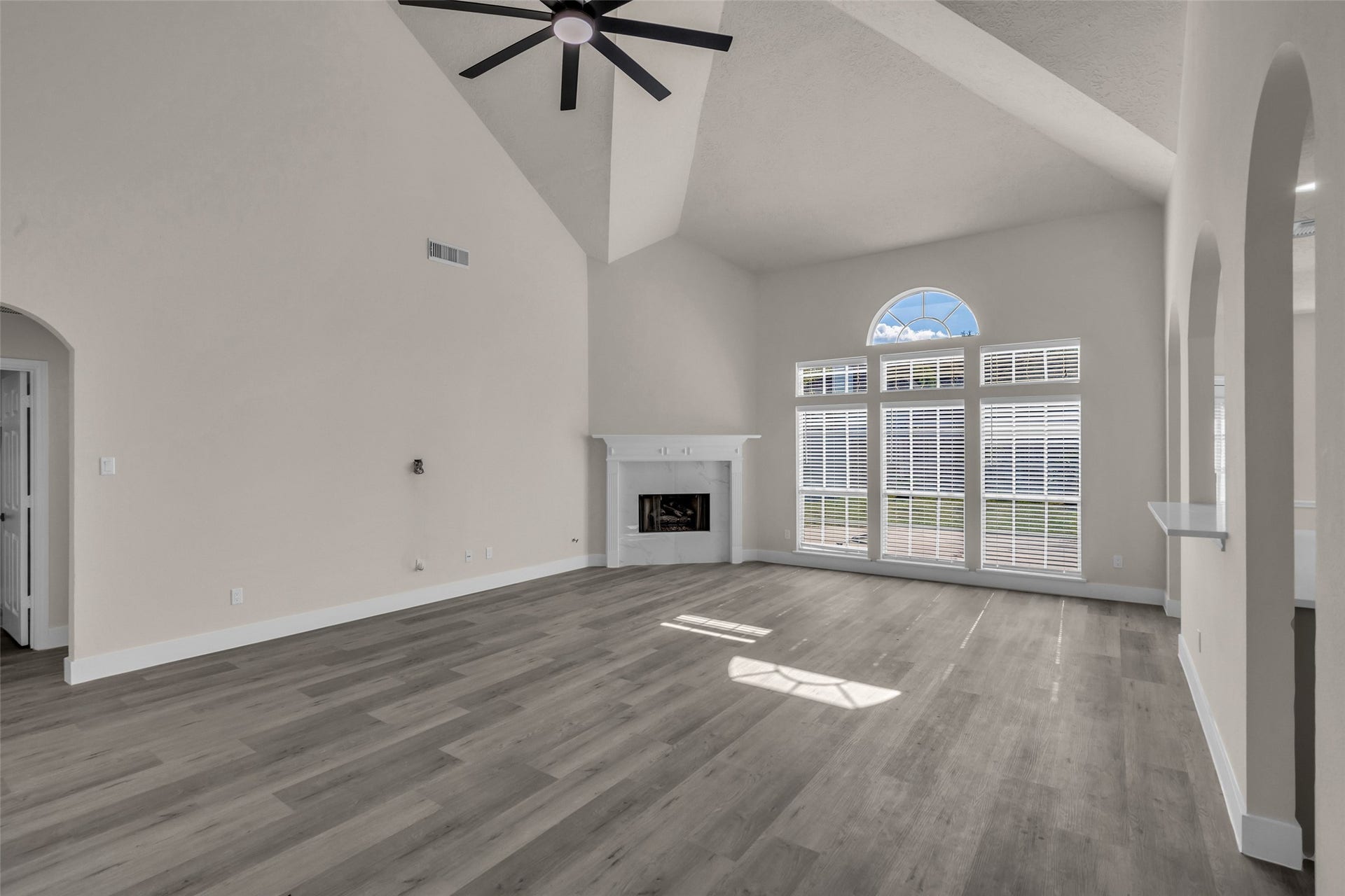 6110 Four River Drive, Richmond, TX 77469 Spacious living area with high ceilings, elegant arched windows, and a cozy fireplace, complemented by sleek wood flooring and modern finishes.