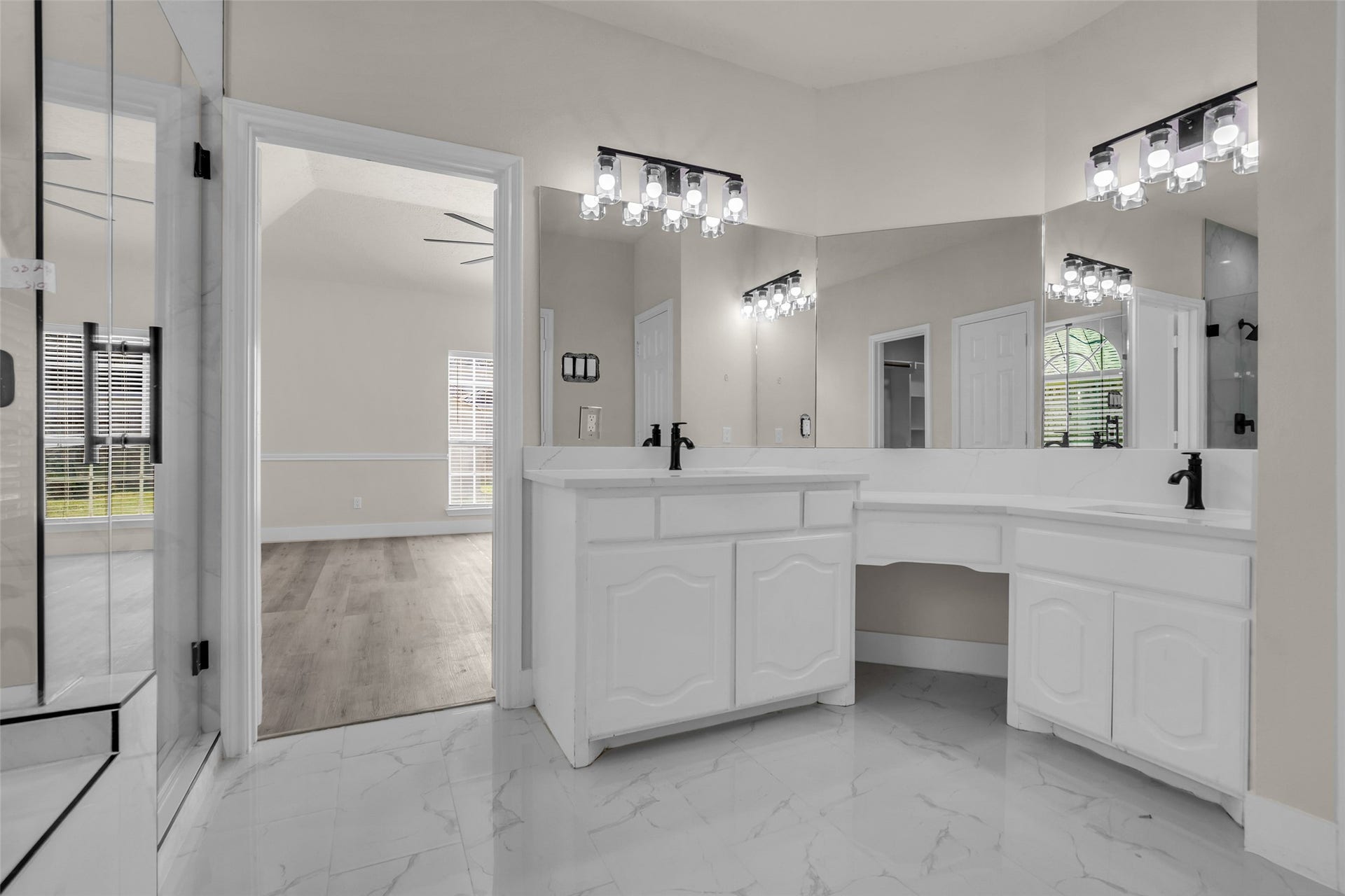 6110 Four River Drive, Richmond, TX 77469 Elegant bathroom featuring dual vanities with modern fixtures, ample counter space, and stylish lighting, seamlessly flowing into a bright room with rich wood flooring.