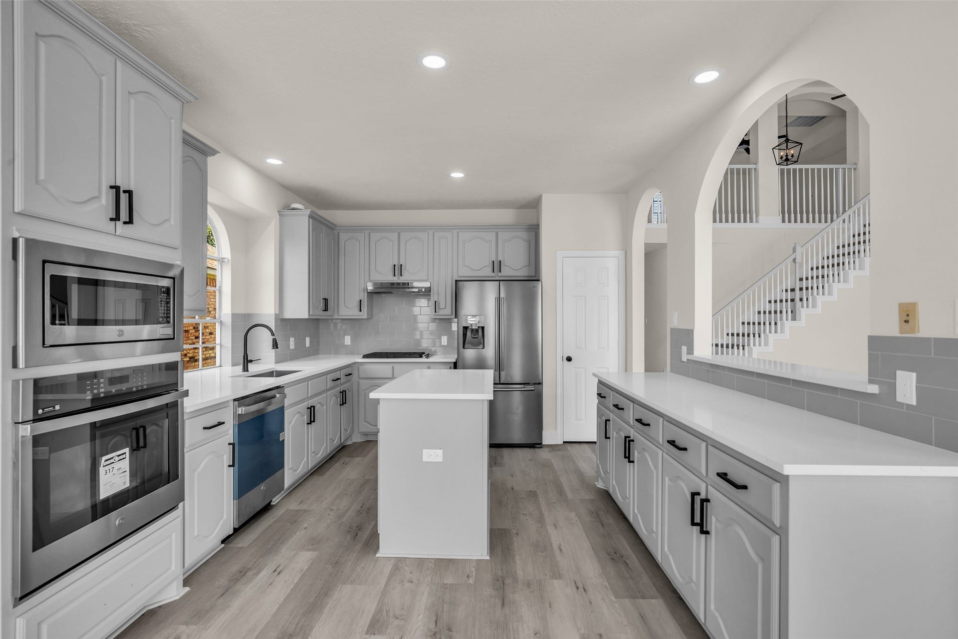 6110 Four River Drive, Richmond, TX 77469 Modern kitchen featuring sleek gray cabinetry, stainless steel appliances, and a spacious island, complemented by stylish arched entries and abundant natural light.