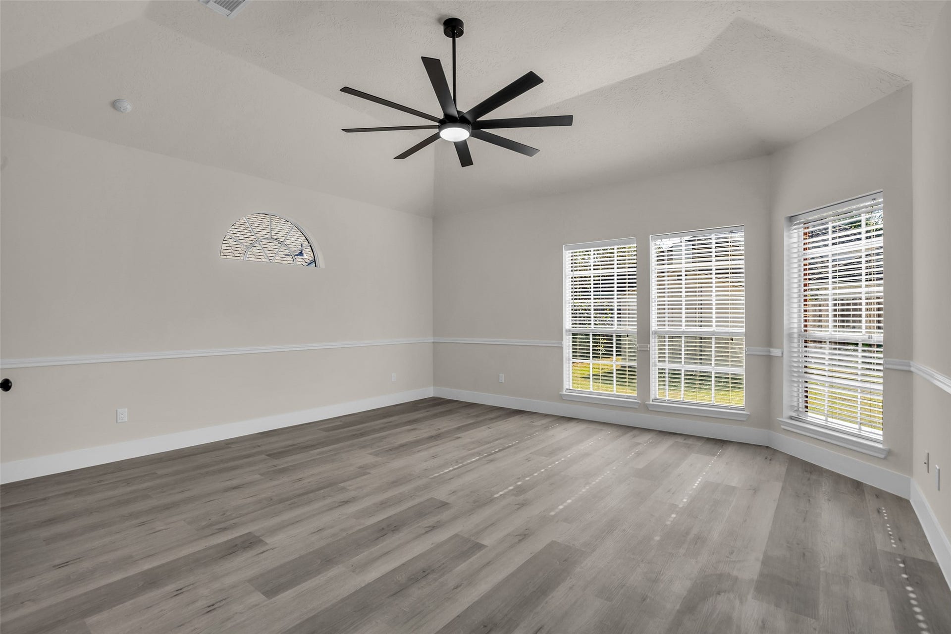 6110 Four River Drive, Richmond, TX 77469 Spacious primary bedroom with elegant wood flooring, abundant natural light from large windows, and a modern ceiling fan adding a stylish touch.