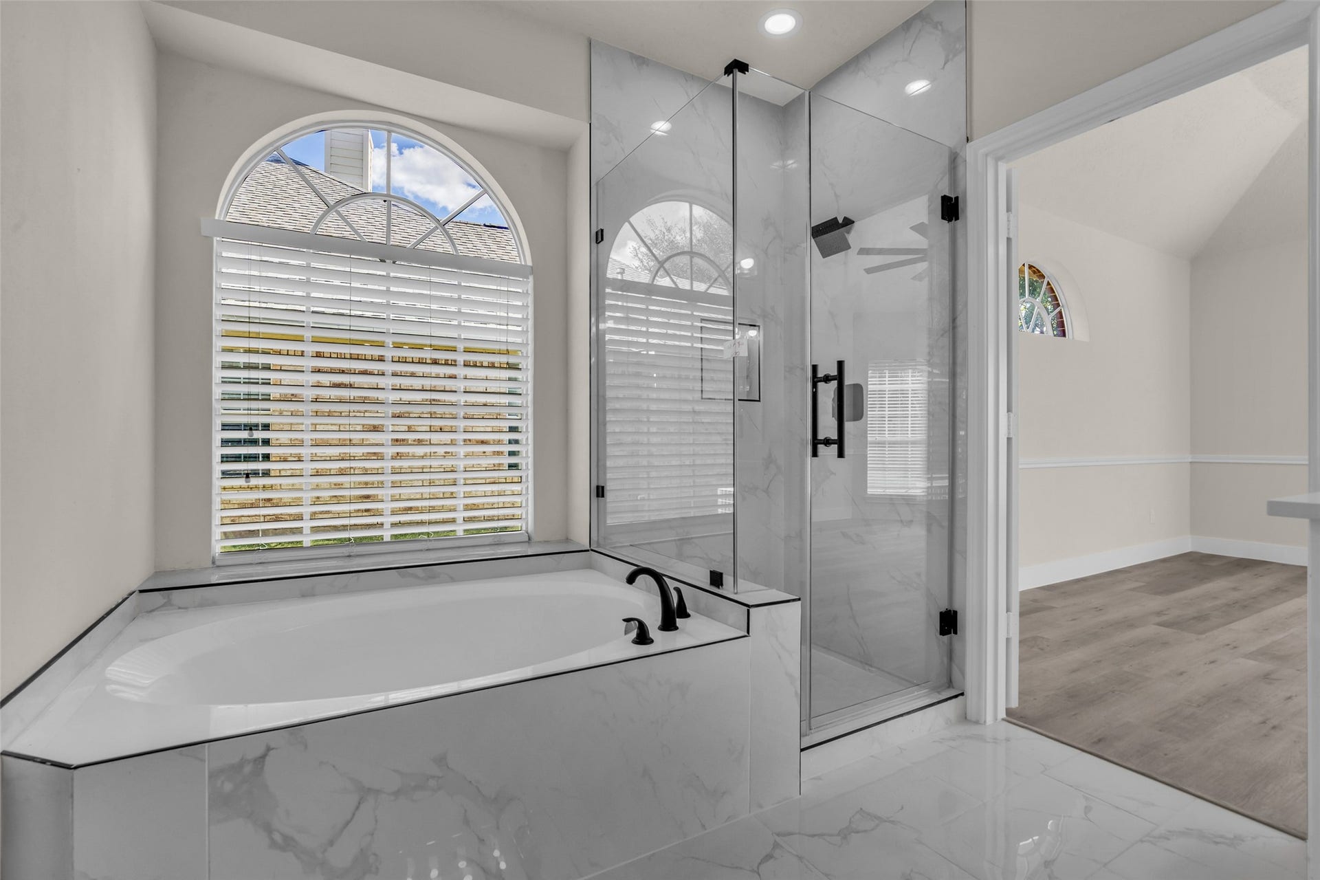 6110 Four River Drive, Richmond, TX 77469 Luxurious bathroom featuring a sleek glass-enclosed shower and a spacious soaking tub, complemented by elegant marble tile and arched windows for natural light.