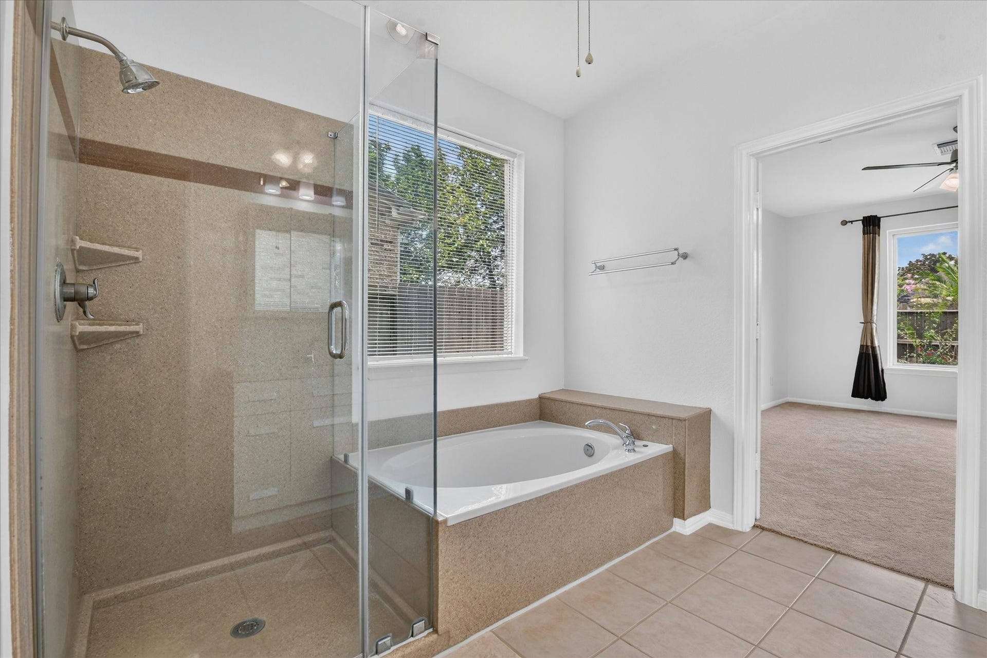 4610 Misty Morning Court, Missouri City, TX 77459 This photo showcases another view of the modern primary bathroom featuring a glass-enclosed shower and a separate bathtub. Natural light streams through a window, enhancing the spacious feel. The bathroom connects to a carpeted primary bedroom with large windows and ceiling fan, providing a bright and airy atmosphere.