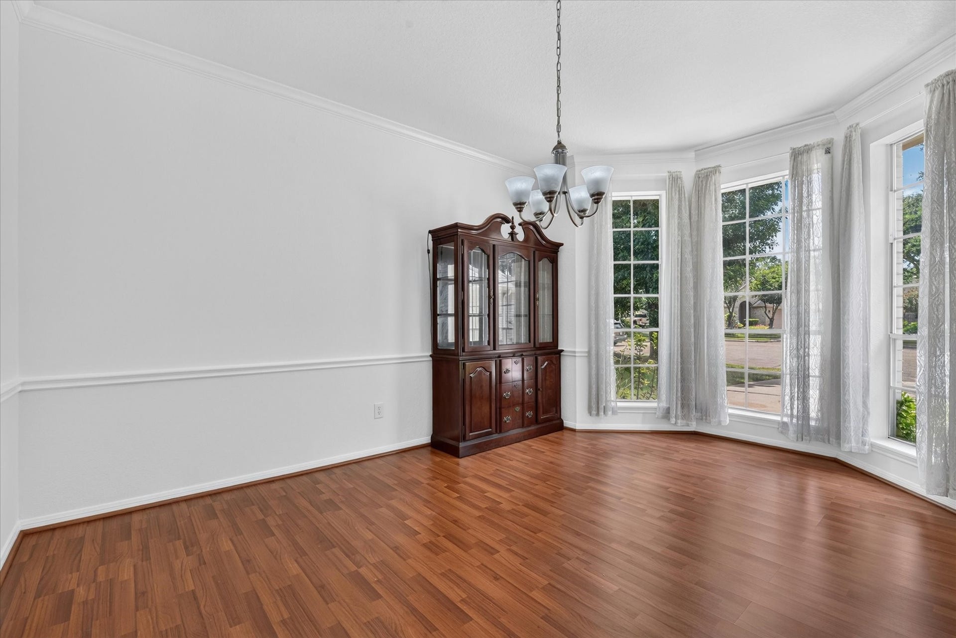 4610 Misty Morning Court, Missouri City, TX 77459 A bright dining area with large bay windows, hardwood floors, and a classic chandelier. The space features a wooden china cabinet and neutral walls, creating an inviting atmosphere.