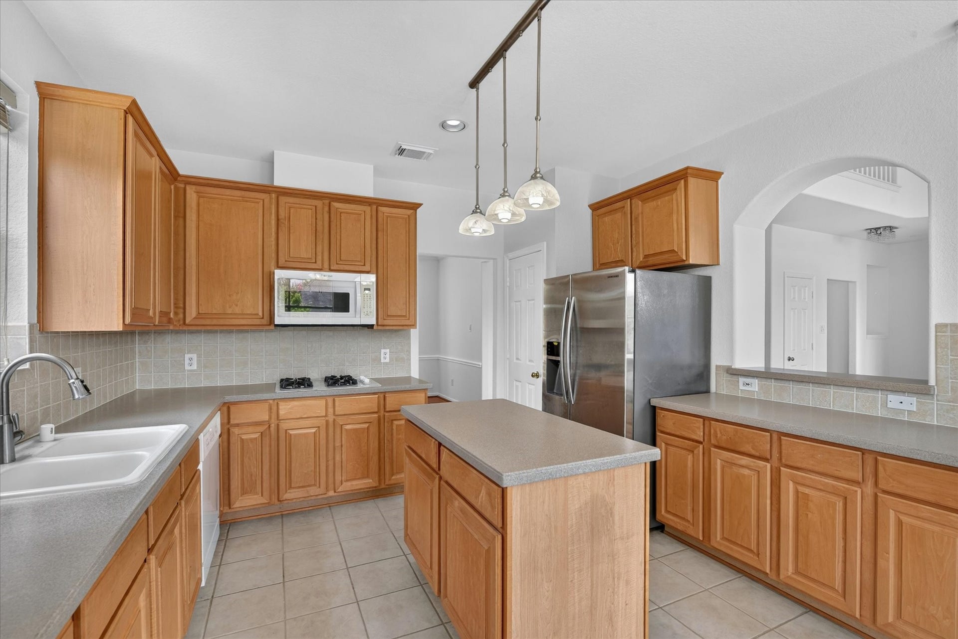 4610 Misty Morning Court, Missouri City, TX 77459 This kitchen features warm wood cabinetry, a central island, and stainless steel appliances, including a double-door refrigerator. It has a modern light fixture and ample counter space, complemented by a tiled backsplash and floor.