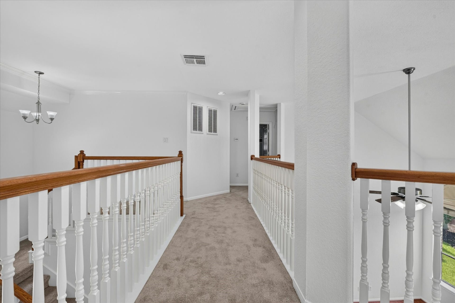 4610 Misty Morning Court, Missouri City, TX 77459 This photo shows a bright, carpeted upstairs hallway with white walls and traditional wooden railing. The space is open with a view of a chandelier and a ceiling fan, creating an airy and inviting atmosphere.