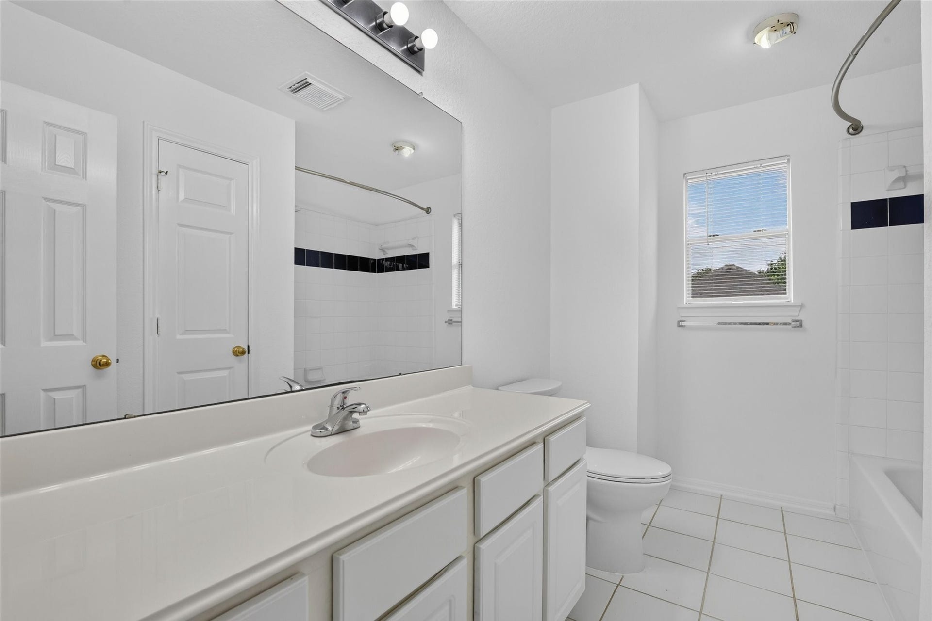 4610 Misty Morning Court, Missouri City, TX 77459 Bright, modern full bathroom with white tiles, a large mirror, and a spacious countertop. Features a bathtub with shower, a window for natural light, and sleek fixtures.