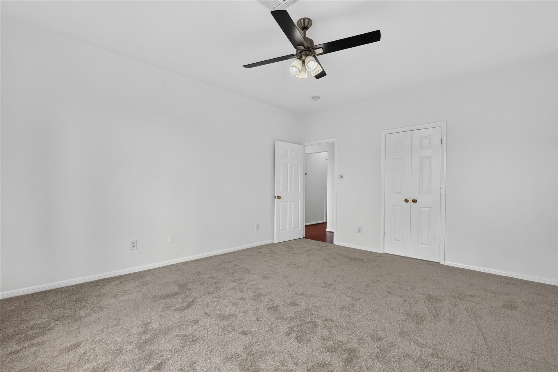 4610 Misty Morning Court, Missouri City, TX 77459 This photo features a spacious bedroom with neutral carpeting, white walls, and a ceiling fan. The room includes a closet with double doors and an open door leading to a hallway, offering a bright and clean space ready for customization.