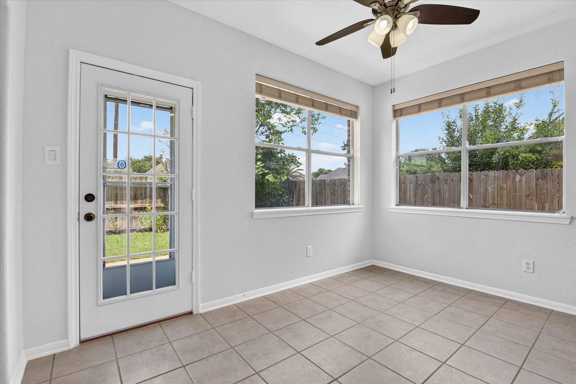 4610 Misty Morning Court, Missouri City, TX 77459 Bright, tiled room with large windows and a glass door leading to a fenced backyard. It features a ceiling fan and neutral paint, offering a clean, airy feel. Ideal for a breakfast nook or sunroom.