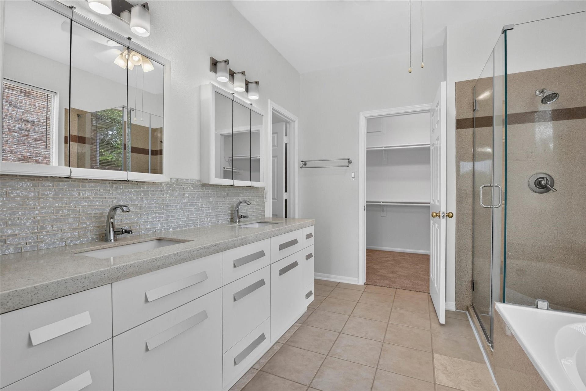 4610 Misty Morning Court, Missouri City, TX 77459 This modern primary bathroom features a double vanity with sleek mirrors and ample storage. It includes a glass-enclosed shower and a large walk-in closet, offering both style and functionality.