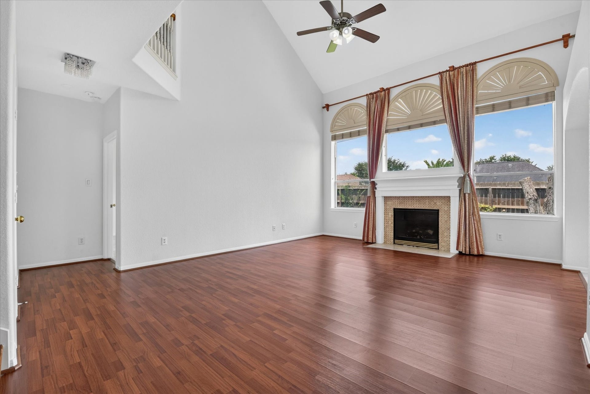 4610 Misty Morning Court, Missouri City, TX 77459 This spacious living room features high ceilings, elegant hardwood floors, and large arched windows for natural light. A central fireplace adds warmth, while a ceiling fan provides comfort.